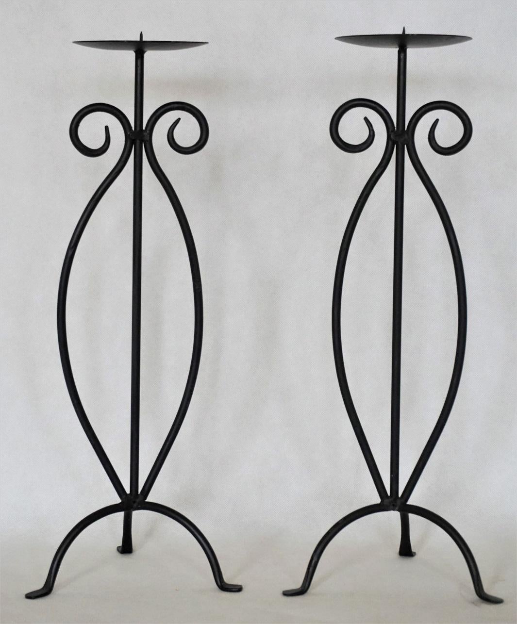 Pair of wrought iron candleholders rised on tripod base, black painted.
Measures:
Height 17.50 in (44.5 cm)
Width/Depth 6.50 in (16.5 cm).
 