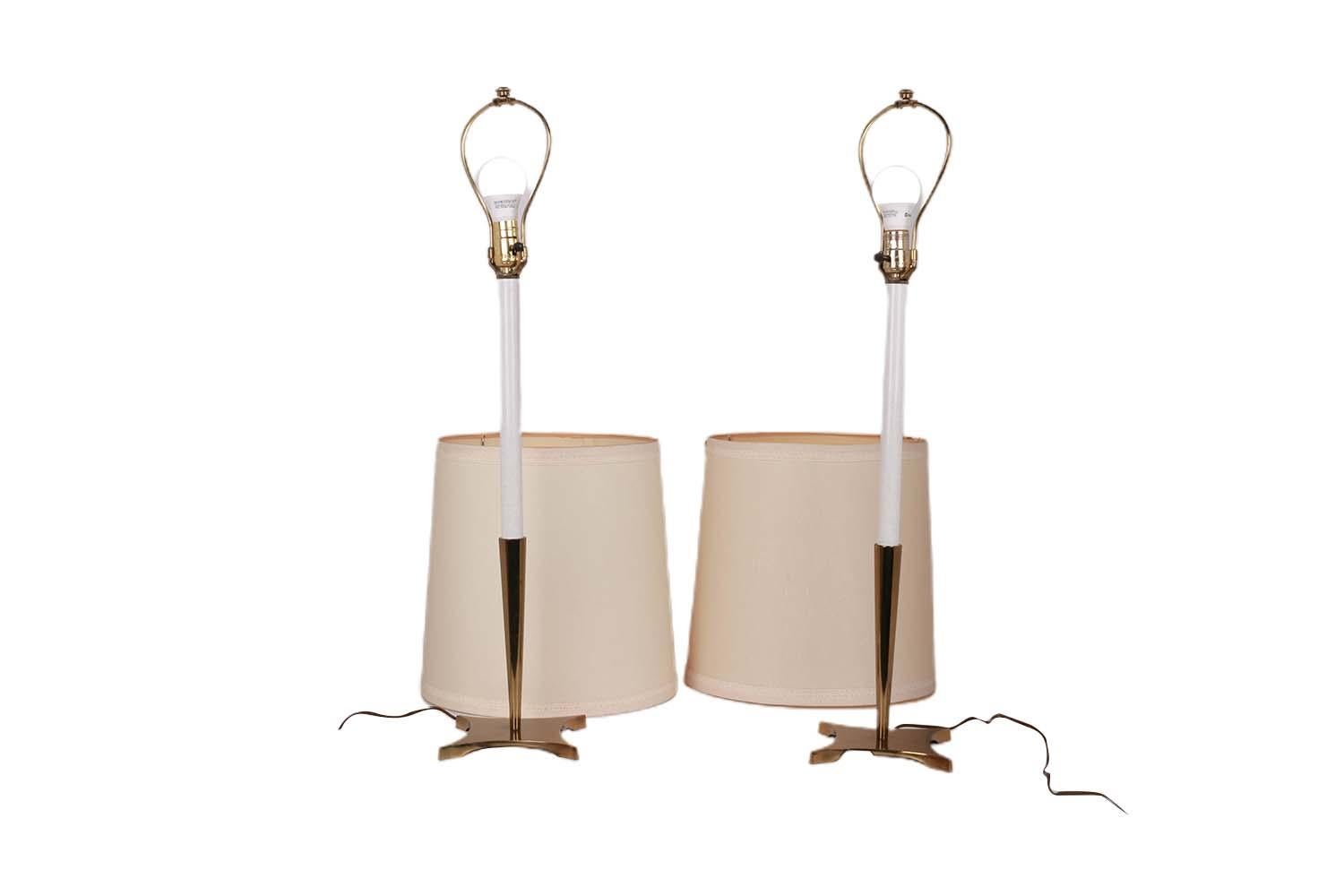 A beautiful pair of tall modernist solid brass candlestick buffet table lamps with original shades by designer Tommi Parzinger for Stiffel, circa 1970's. They feature brass four-point star bases below tapered brass candle holders and white enameled