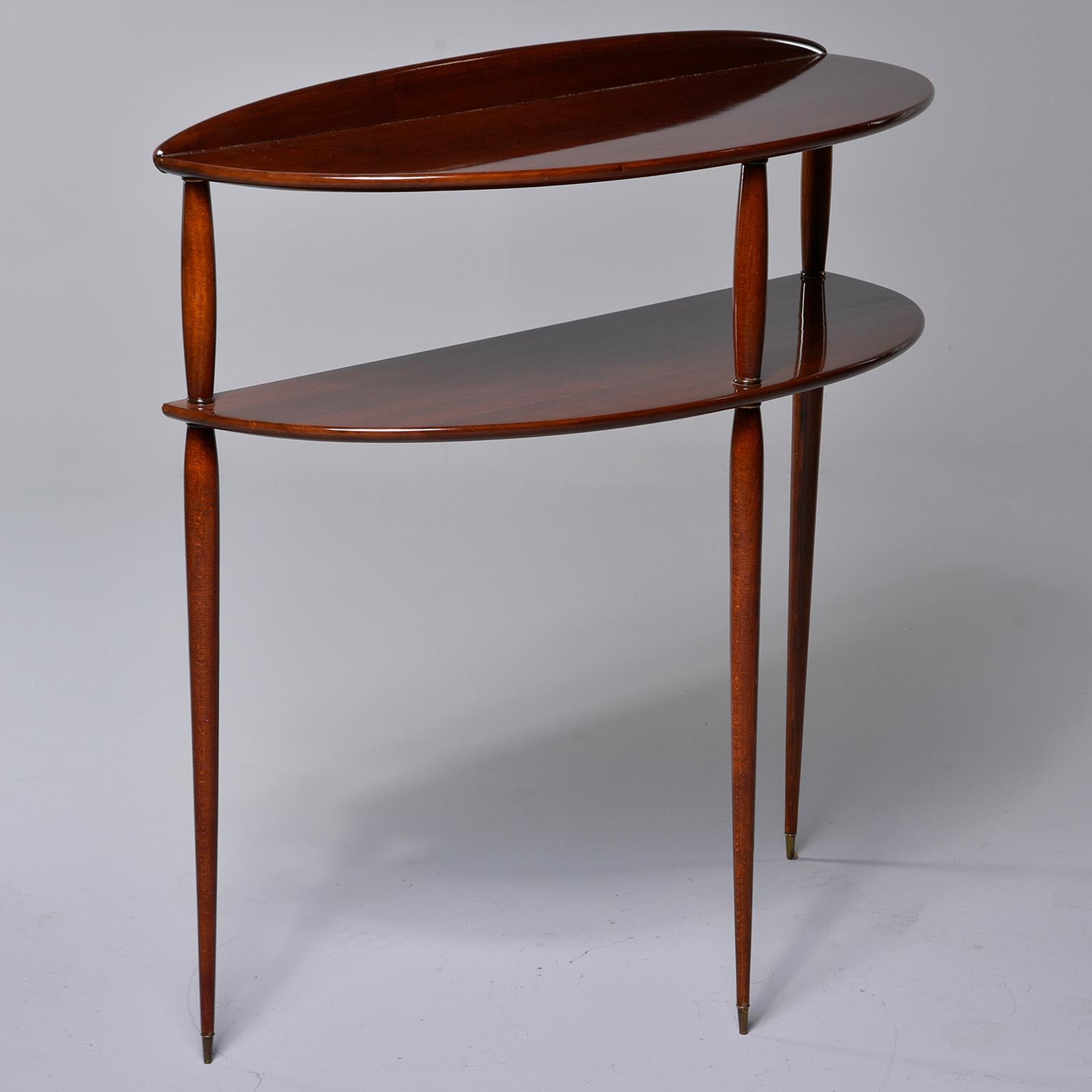 Two-tier palisander console features a demilune shaped tabletop and lower shelf and slender, tapered legs with brass-capped feet, circa 1960. Found in Italy, unknown maker.