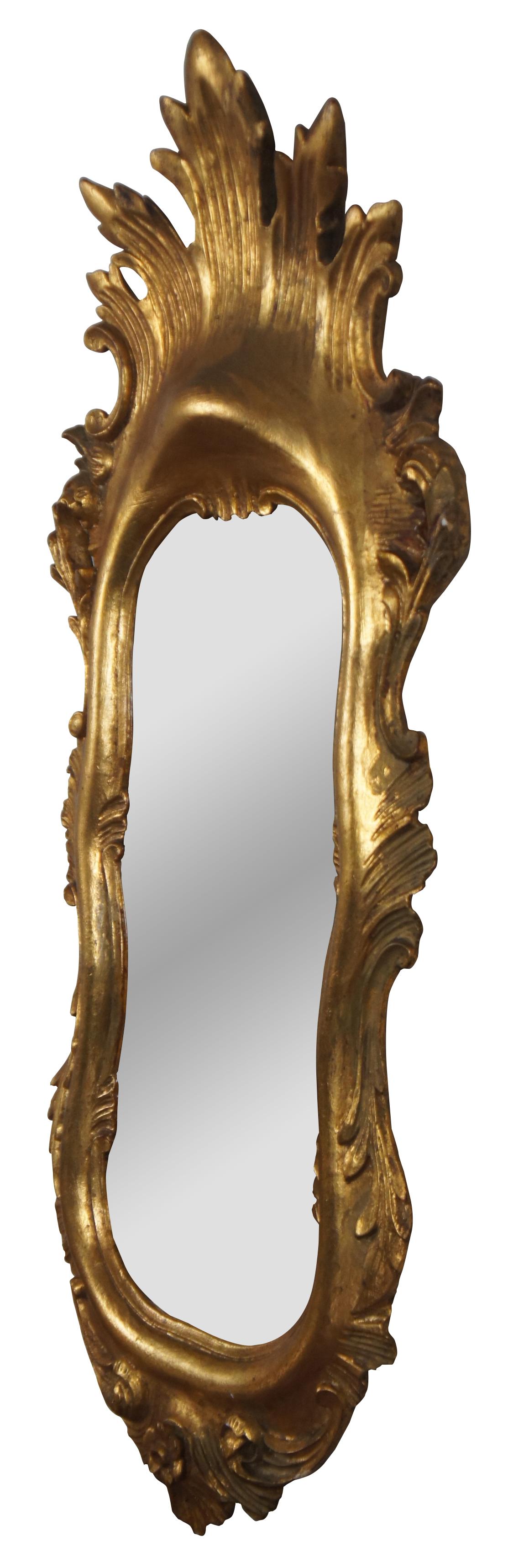 Vintage Italian rococo / baroque / Florentine oval gilt wall vanity mirror by Palmira Art Company, with a motif of scrolling leaves and a splash shape at the crest.

Measures: 12.5” x 2” x 30” / mirror - 6.5” x 16.25” (width x depth x height).
 