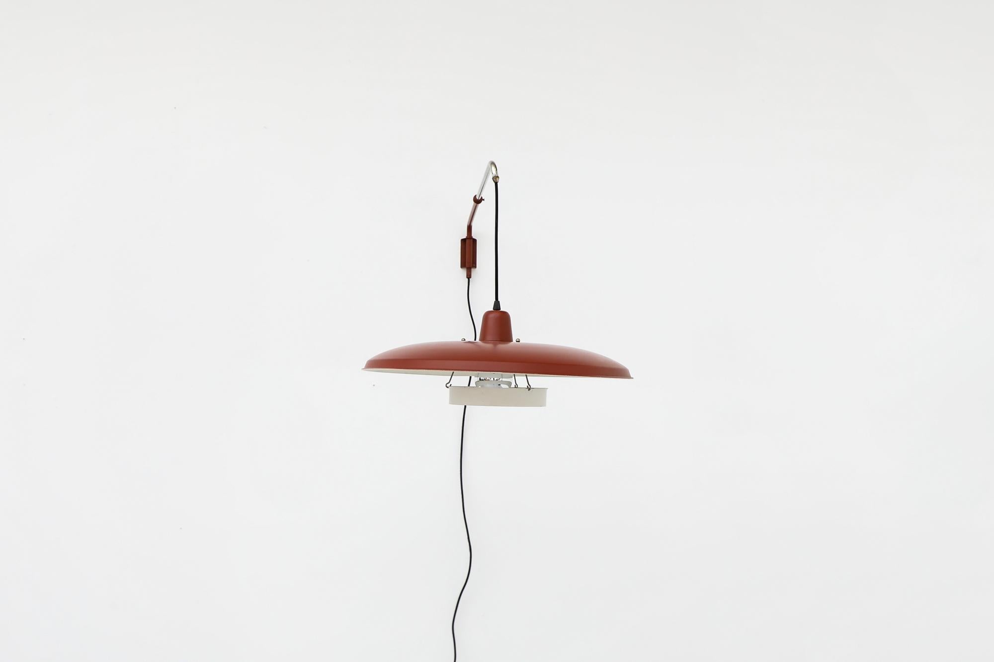 Gorgeous, mid century, ‘Panama’ style wall mounted lamp with brick red enameled metal shade and articulating arm. Position Adjustment is made using the red key on the wall plate. New diffuser. In otherwise good, original condition with some wear.
