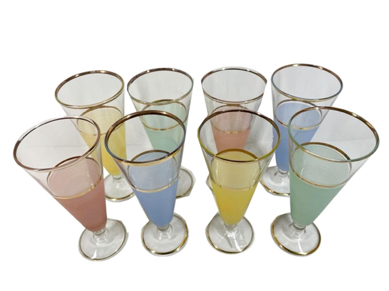 Eight Mid-Century Modern pilsner glasses of taper form, color-frosted lower two thirds below clear tops with 22k gold accent, supported on a ball stem above a raised dome foot. The set is comprised of two each, pink, yellow, green and blue.