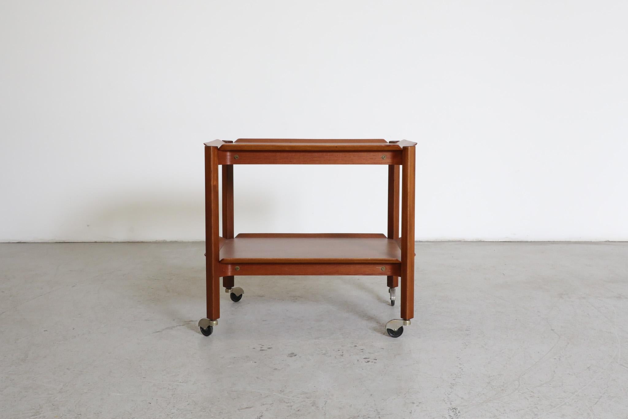 Mid-Century 2 tiered teak rolling cart designed by Dutch post-war icon Cees Braakman for Pastoe. Beautiful and delicate teak trays with upturned edges and clipped corners hat rest between the dark teak frame. It can be said that Braakman was almost