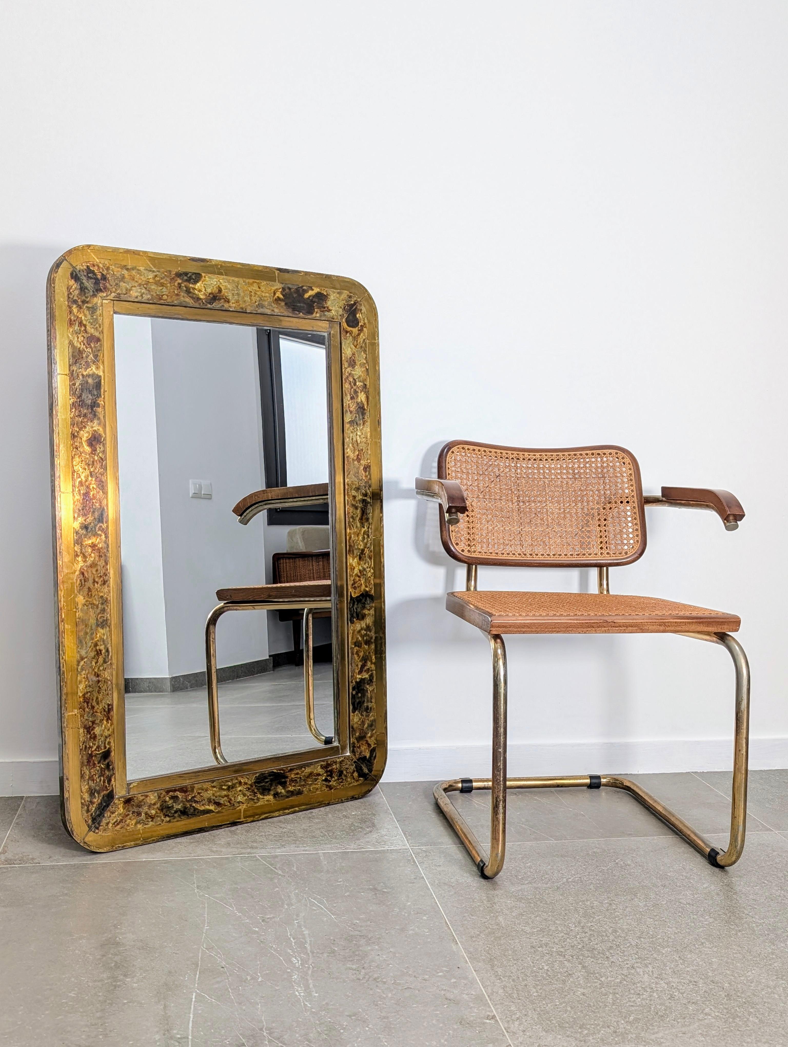 Elegante specchio con cornice in ottone patinato con accenti dorati, risalente agli anni Sessanta. La superficie rivela una patina ricca e originale che ricorda da vicino i motivi organici e profondi del legno di radica, conferendogli una