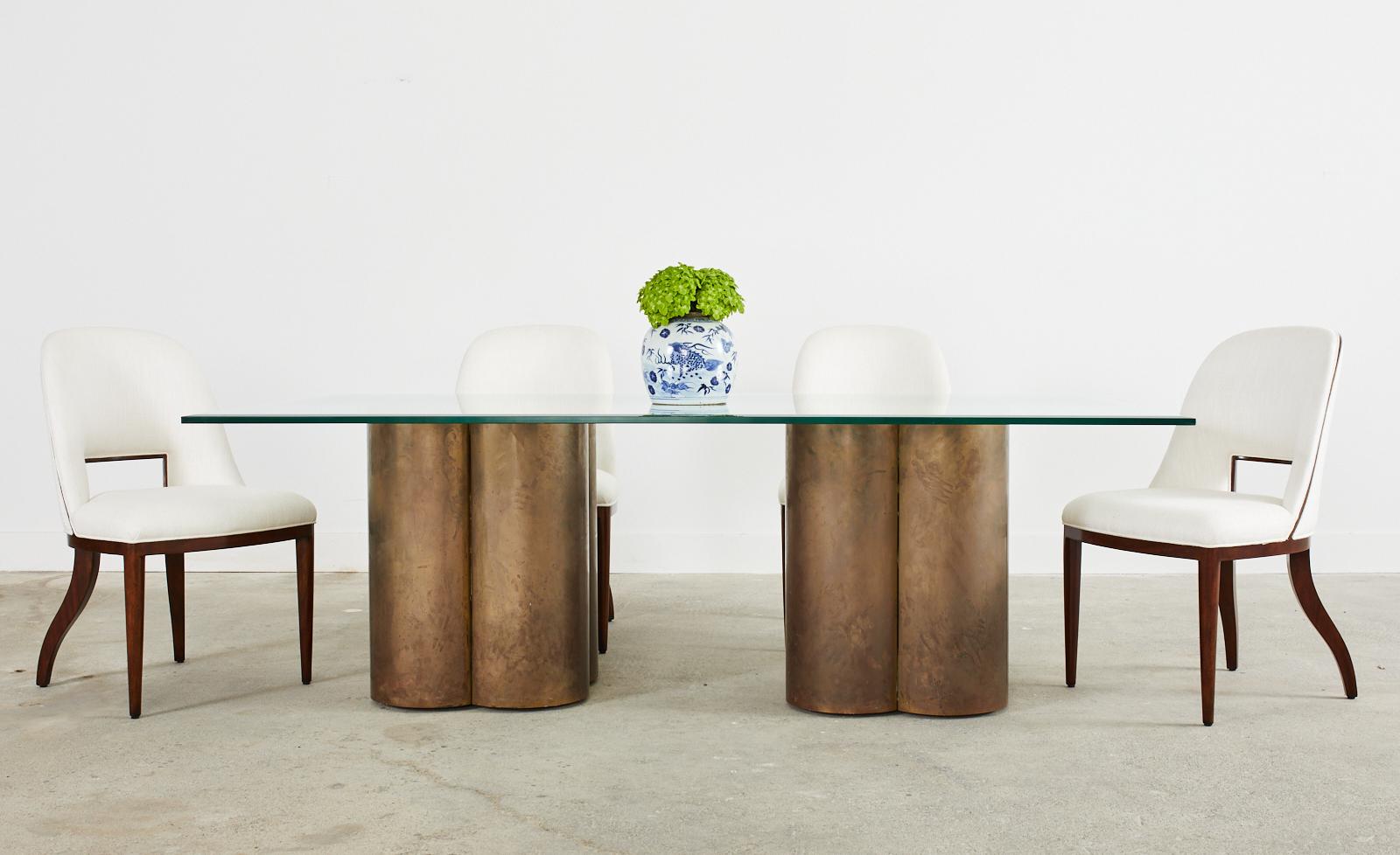 Fascinating mid-century modern dining table featuring two massive pedestals clad in patinated brass having quatrefoil or clover forms. The pedestals are unsigned however, they are crafted in the style and manner of Bernard Rohne for Mastercraft and