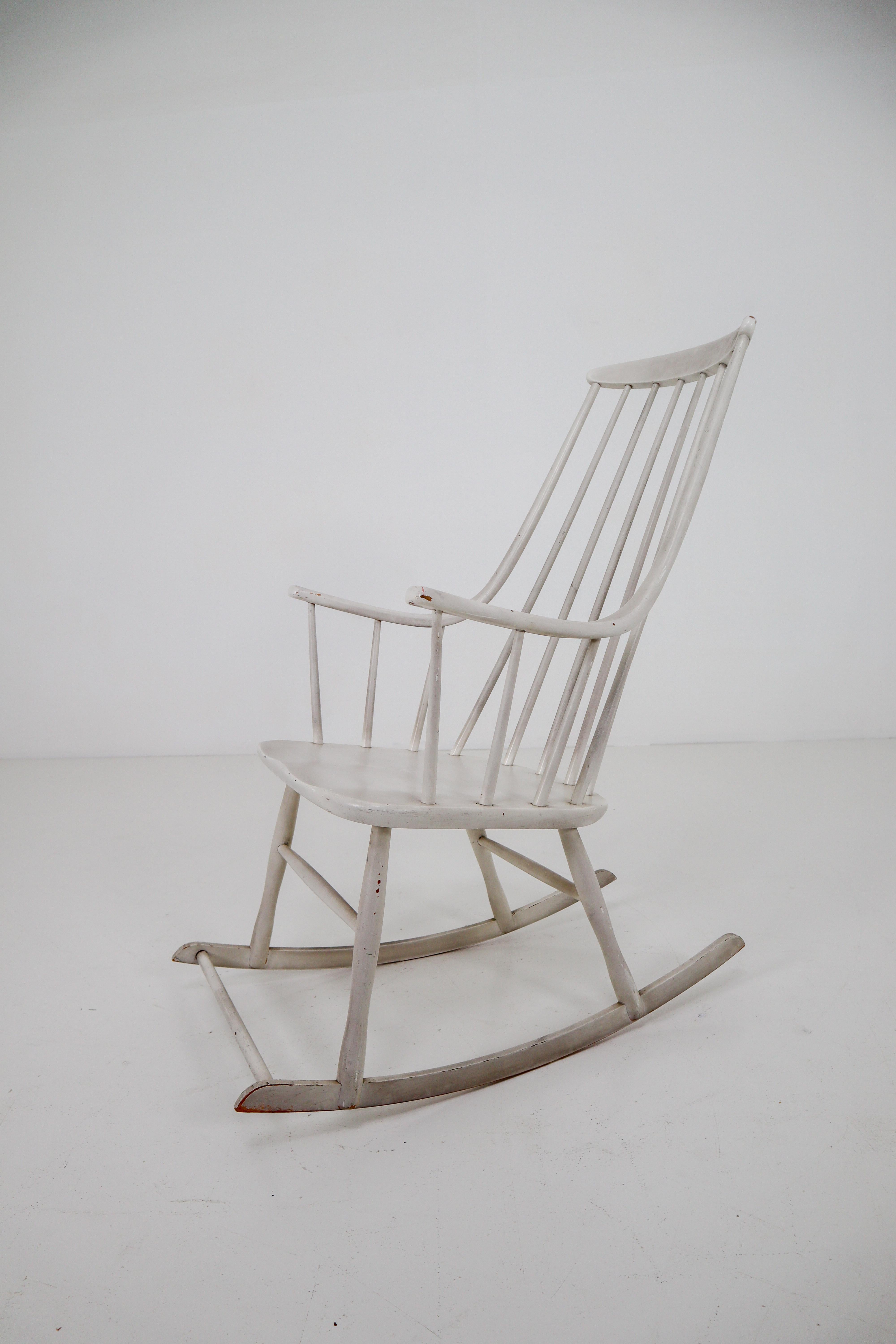 Wonderful French rocking produced in the 1950s, in light-gray-white painted beech with solid wood seat, features a tall spindle back, gracefully curvaceous arms and runners. The condition of the rocking chair is very good with minor signs of age and