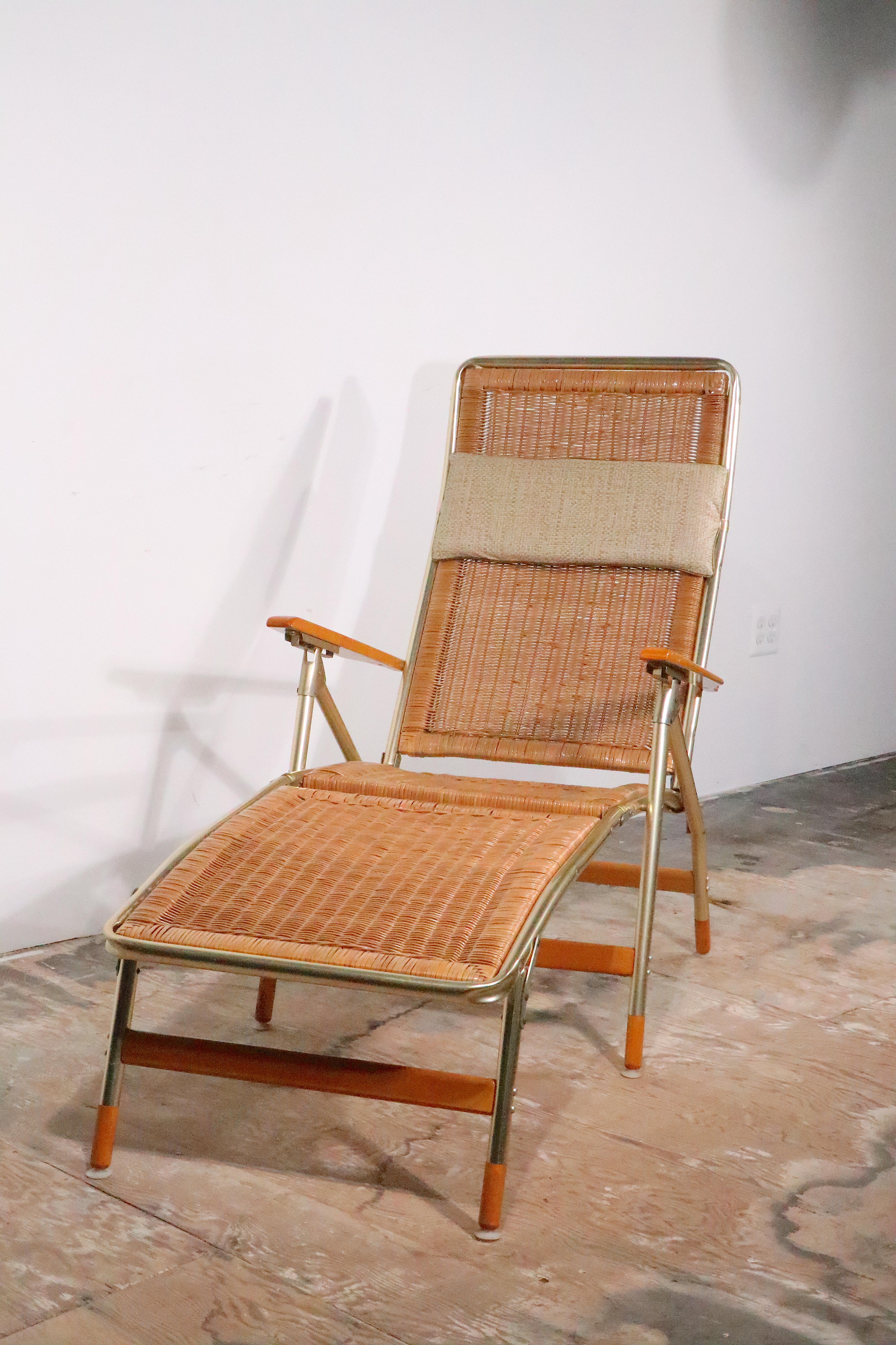 Voguish Mid Century patio, poolside, garden chaise lounge, by the Telescopce Chair Company. The chaise is constructed of an anodized gold tone aluminum frame, with solid wood arms, the continuous back and seat is  composed of plastic faux wicker.