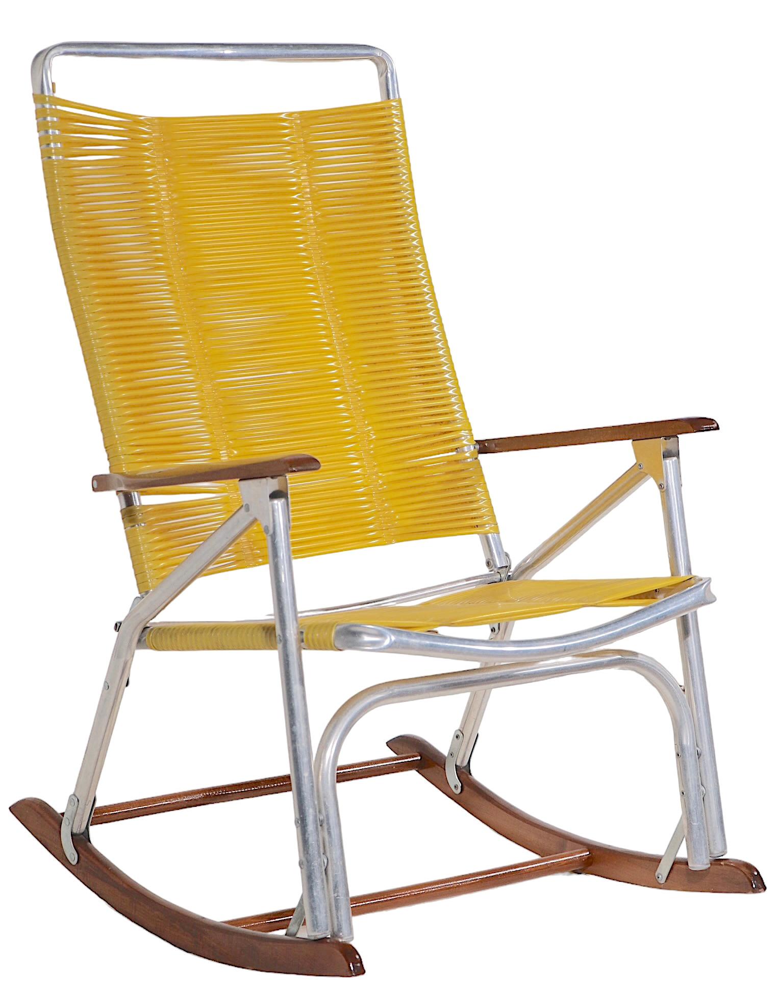 Chic Mid Century  vintage patio, poolside, rocking chair made by the Telescope Chair Company, circa 1950/1970's. The chair features a  bright yellow plastic strap back and seat, wood arm rests and rockers, with a folding tubular aluminum frame. This