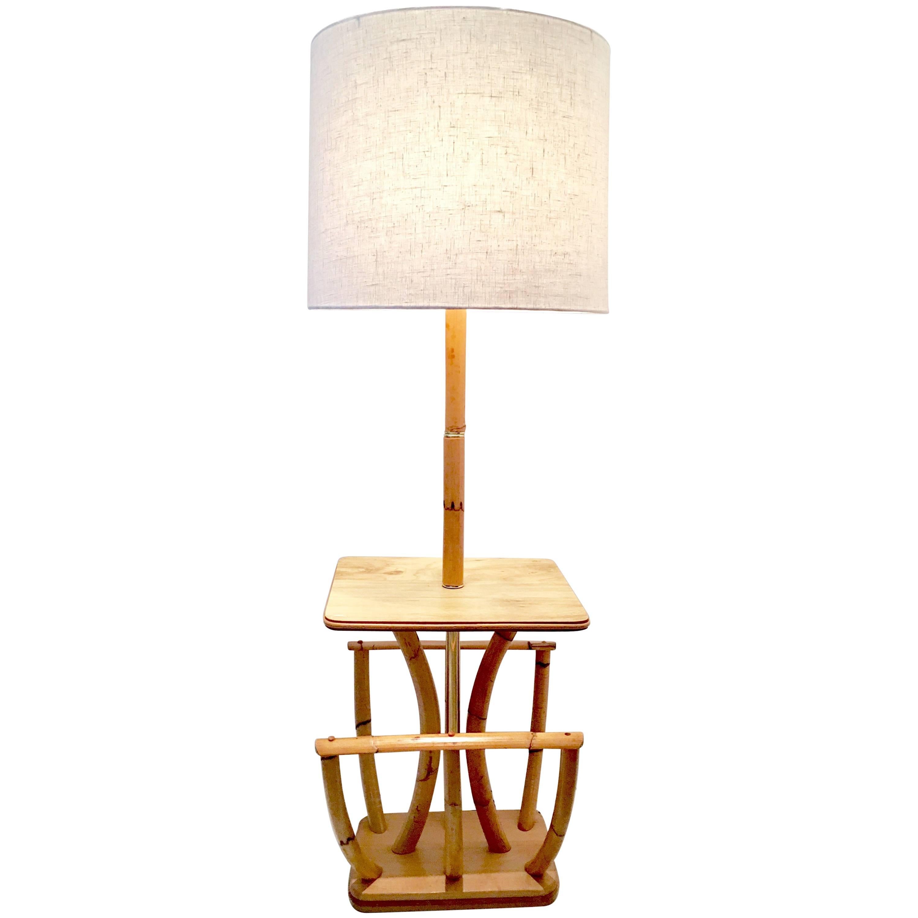1930s Paul Frankl style rattan reed and brass floor table lamp with magazine rack. This unique and rare floor lamp features a center polished brass pole and ring detail with a large magazine rack and mahogany platform base. Includes brass finial and