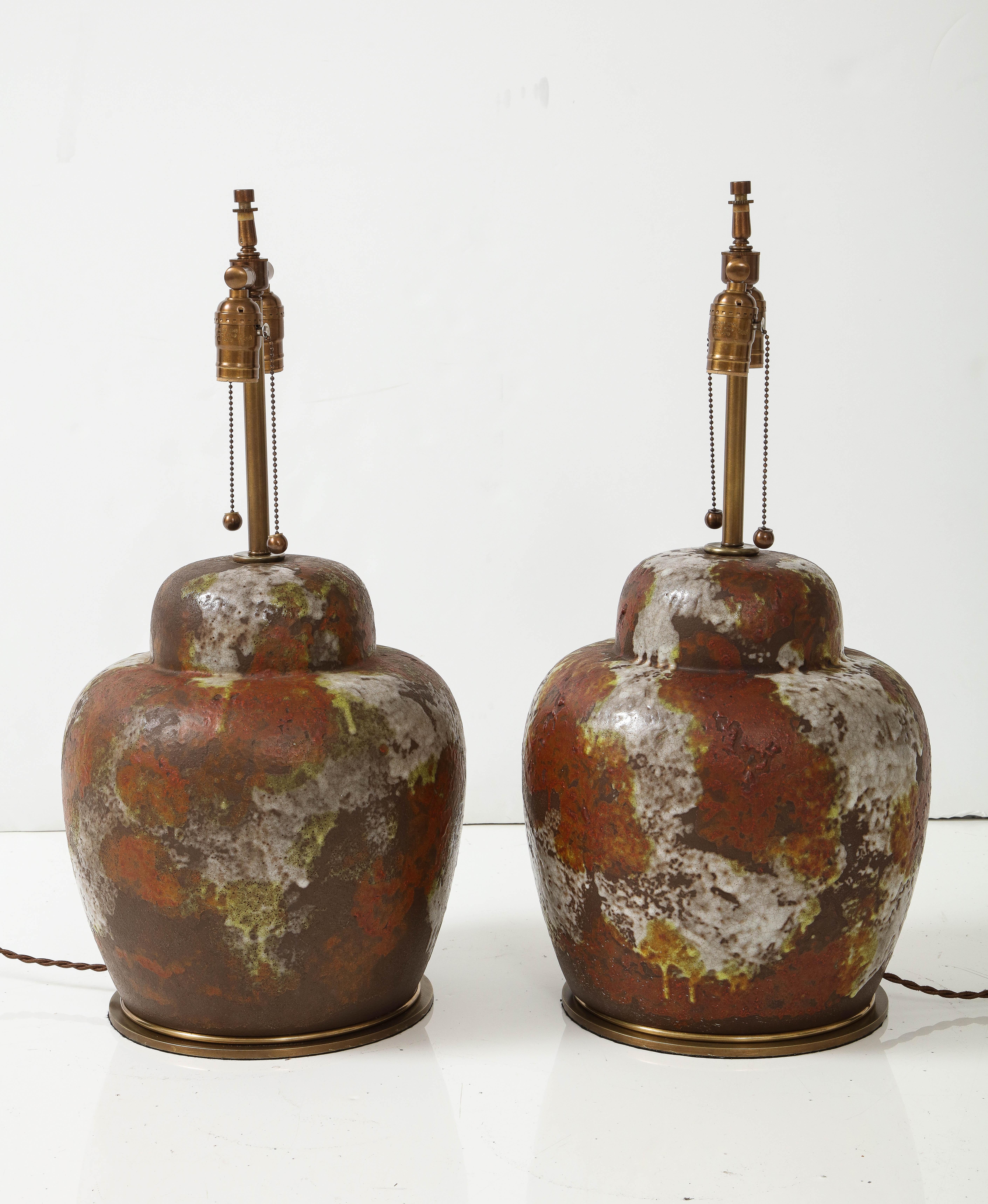 Pair of large scale ceramic ginger jar form lamps featuring a matte mottled glaze in colors of brown, rust, wasabi green and white. Rewired for use in the USA with bronze double pull chain sockets, 75W max each socket, brown knit covered cords.
