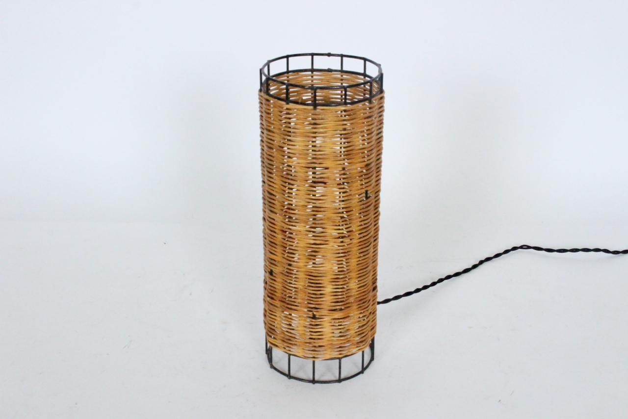 Mid-Century Modern Paul Mayen for Habitat Style Rattan and Wire Table Lamp. Featuring a cylindrical black enameled metal open framework, hand wrapped in woven rattan with exposed Black rim and base. Standard socket. Turn switch to base. Classic.