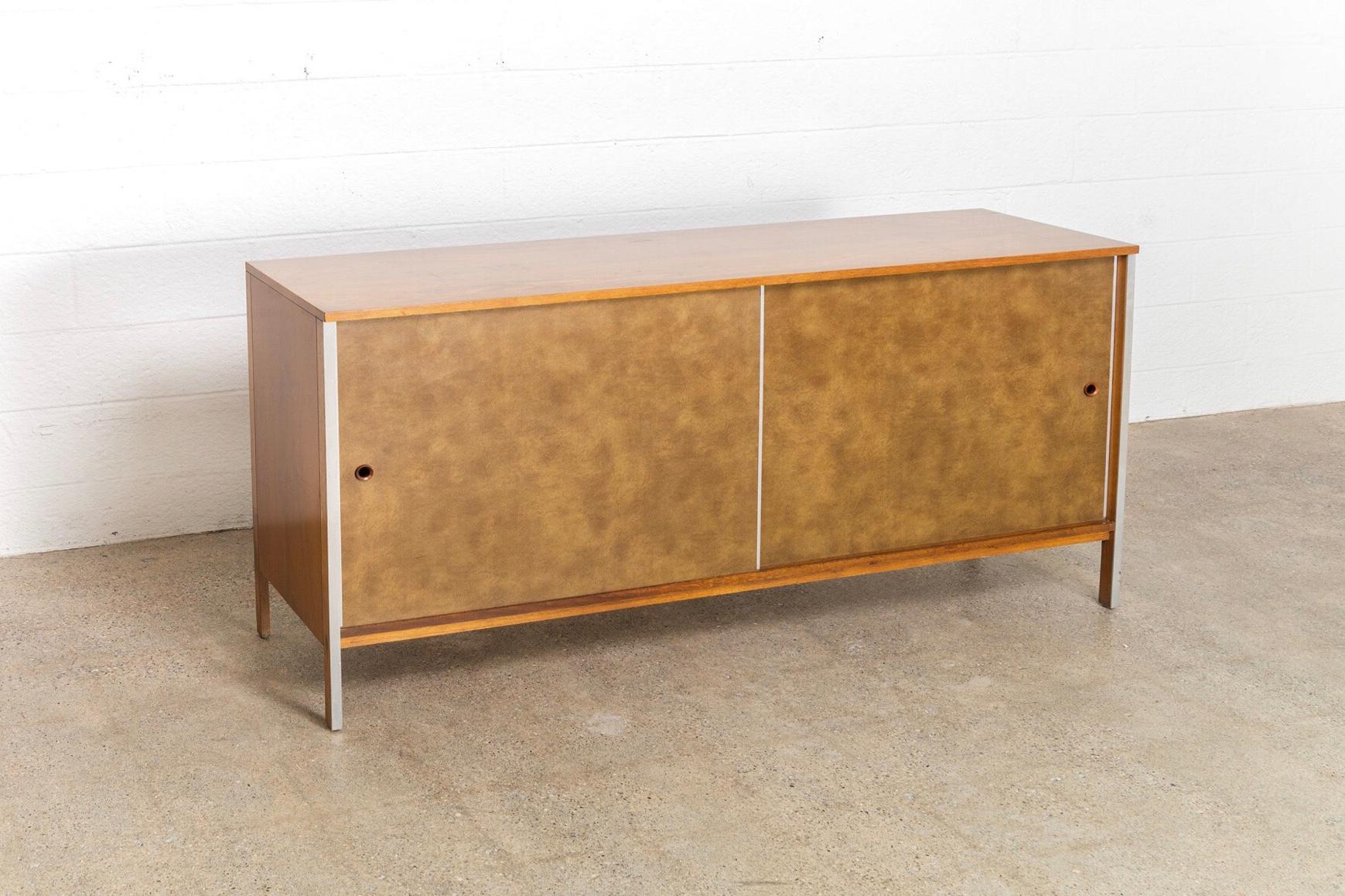 This vintage Mid-Century Modern Paul McCobb walnut credenza was produced by Calvin Furniture, circa 1960. Part of the Linear Group Line, the credenza has sliding leatherette doors opening to two drawers on the left and a spacious storage area on the