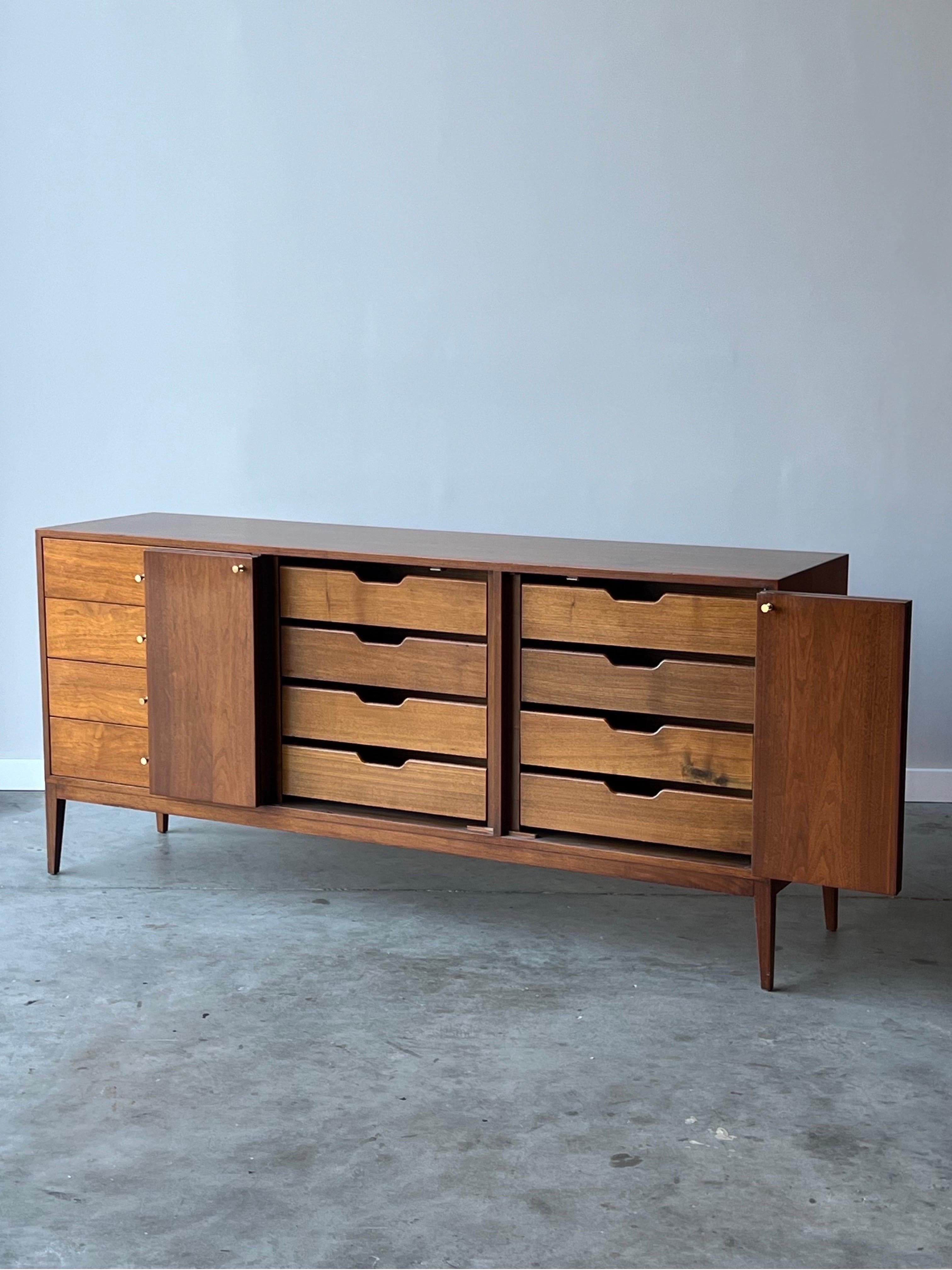 Mid-century long and large dresser in the style of Paul McCobb. This impressive piece is made from walnut and features twelve smooth-sliding drawers. Four drawers frame the left side of the piece accented with brass handles. Two bi-fold doors open