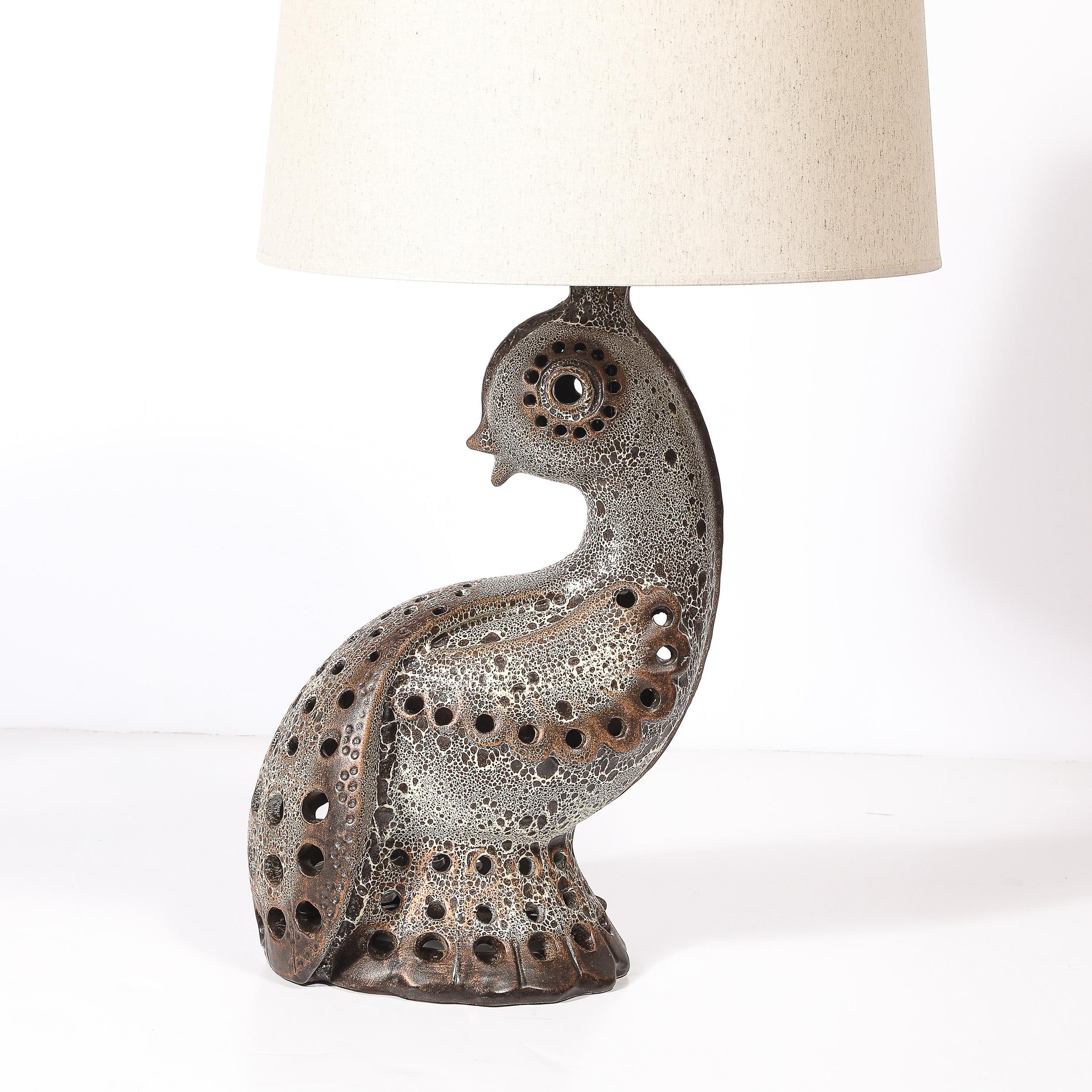 This elegant Mid-Century Modernist table lamp, crafted in France circa 1950, is a captivating blend of artistic form and functional design. The lamp’s ceramic body features a gracefully sculpted silhouette rendered in simplified curved forms,