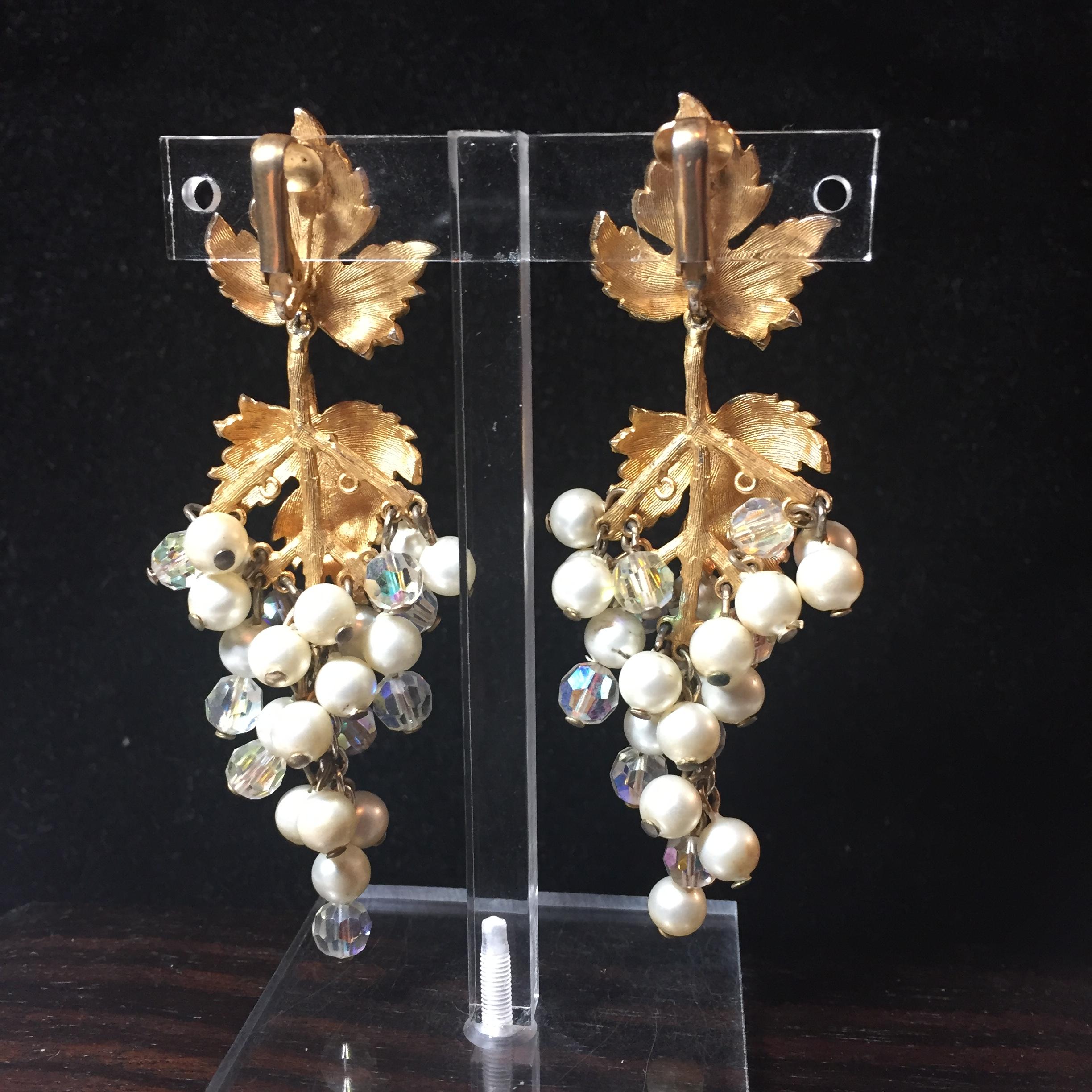 Offered here is a pair of Mid-Century gold-plated dangling clip-back earrings from the 1950s. On the ear is a meticulously detailed grape leaf; dangling from this is another leaf atop a branched structure, from which are suspended multiple glass
