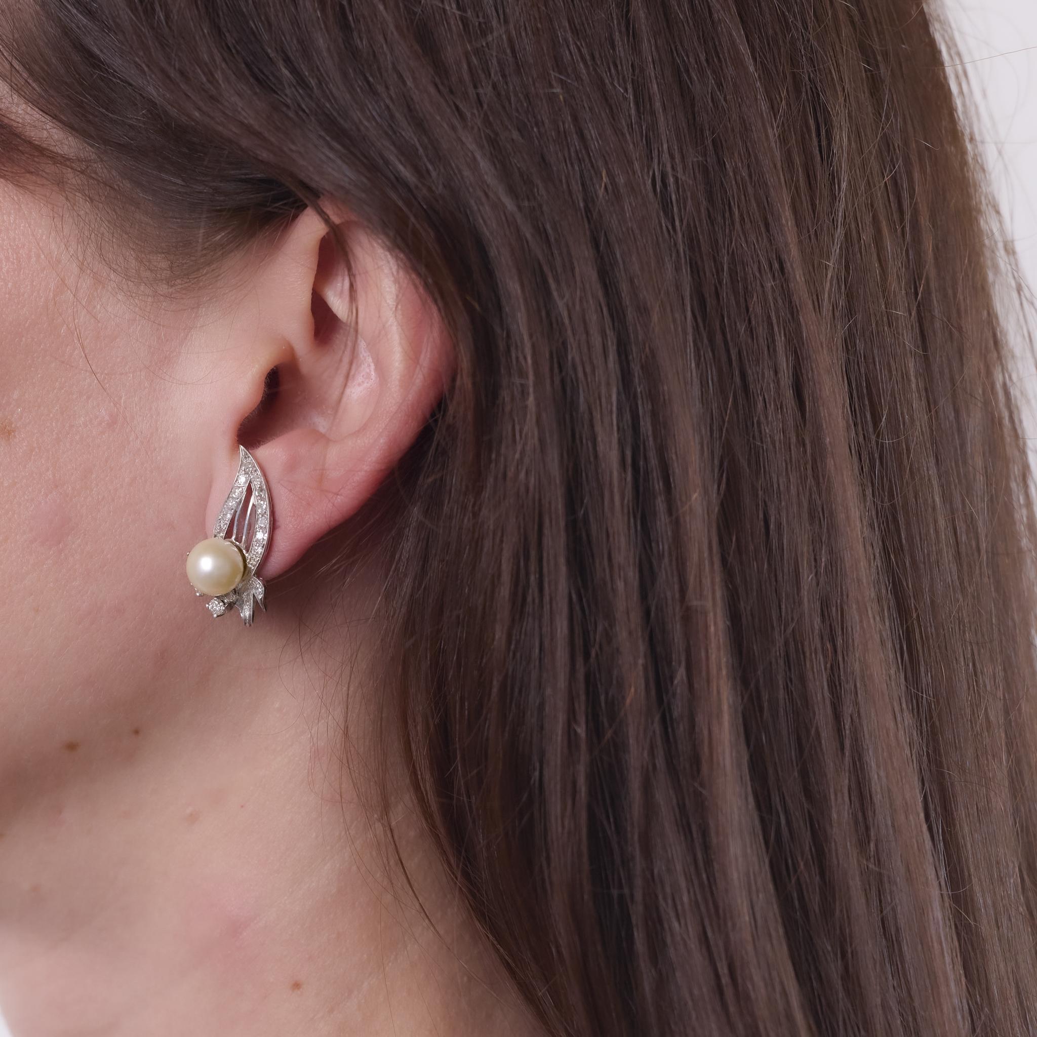 These Mid Century earrings from the 1950s are crafted in 14k white gold and feature two pearls measuring approximately 8.65 mm each. Accented by thirty-eight single cut diamonds totaling approximately 0.60 carats, graded H-I color and I clarity, the