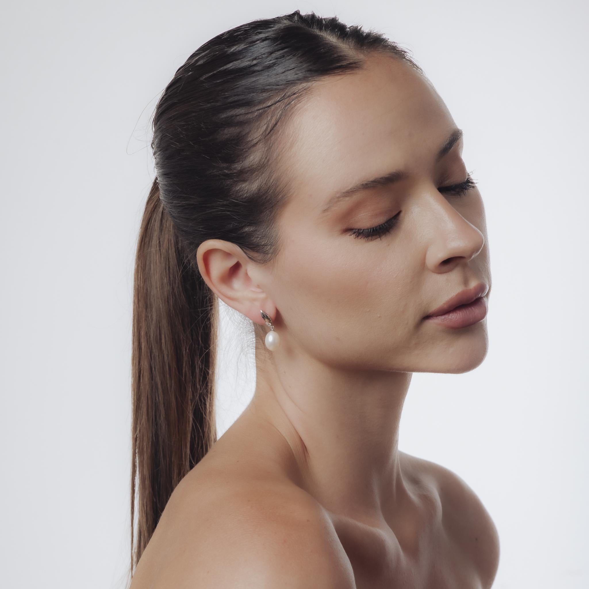 Ces boucles d'oreilles Mid-Century des années 1960 sont réalisées en or blanc 18 carats avec des fonds en or blanc 14 carats. Chaque boucle d'oreille présente une perle lumineuse mesurant environ 11,64 x 9,10 mm, rehaussée de six diamants taille