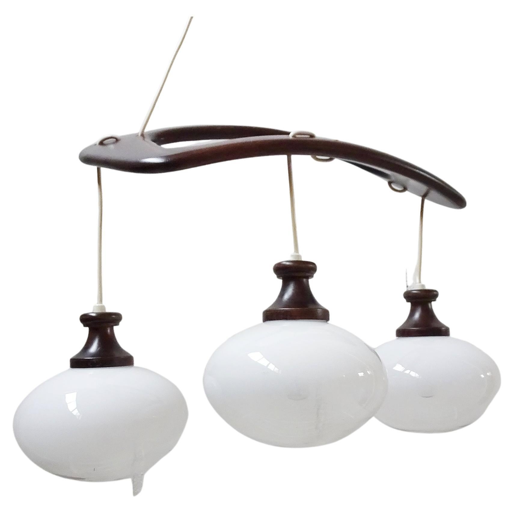 Italian pendant lamp by Mazzega from the 1960s. Shapely mid-century design made of arched teak wood and three glass balls. The semi-tinted glass makes it the ideal pendant lamp above the table.

Lamp socket 3 x E14, the delivery takes place with