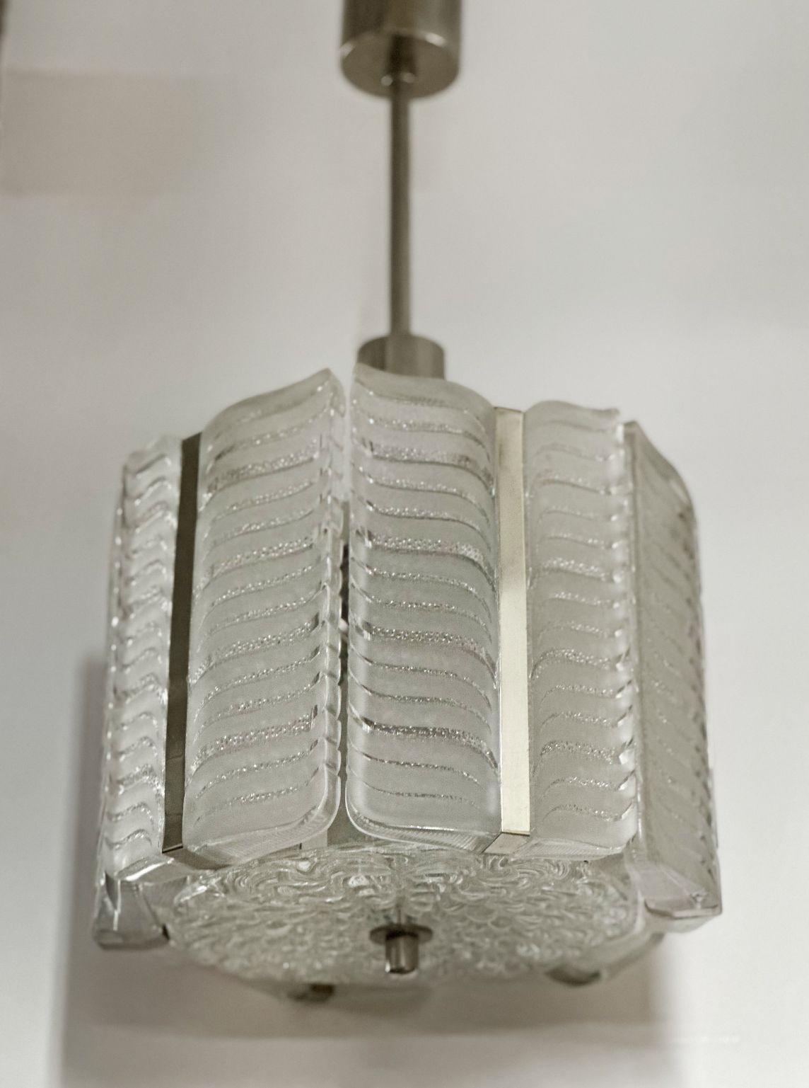 This elegant Austrian chandelier, crafted by Kalmar Vienna in the late 1950s, boasts a nickel-plated metal frame supporting exquisite textured ice glass in a sophisticated Chevron pattern. Its drum-shaped pendant features a round glass disk secured