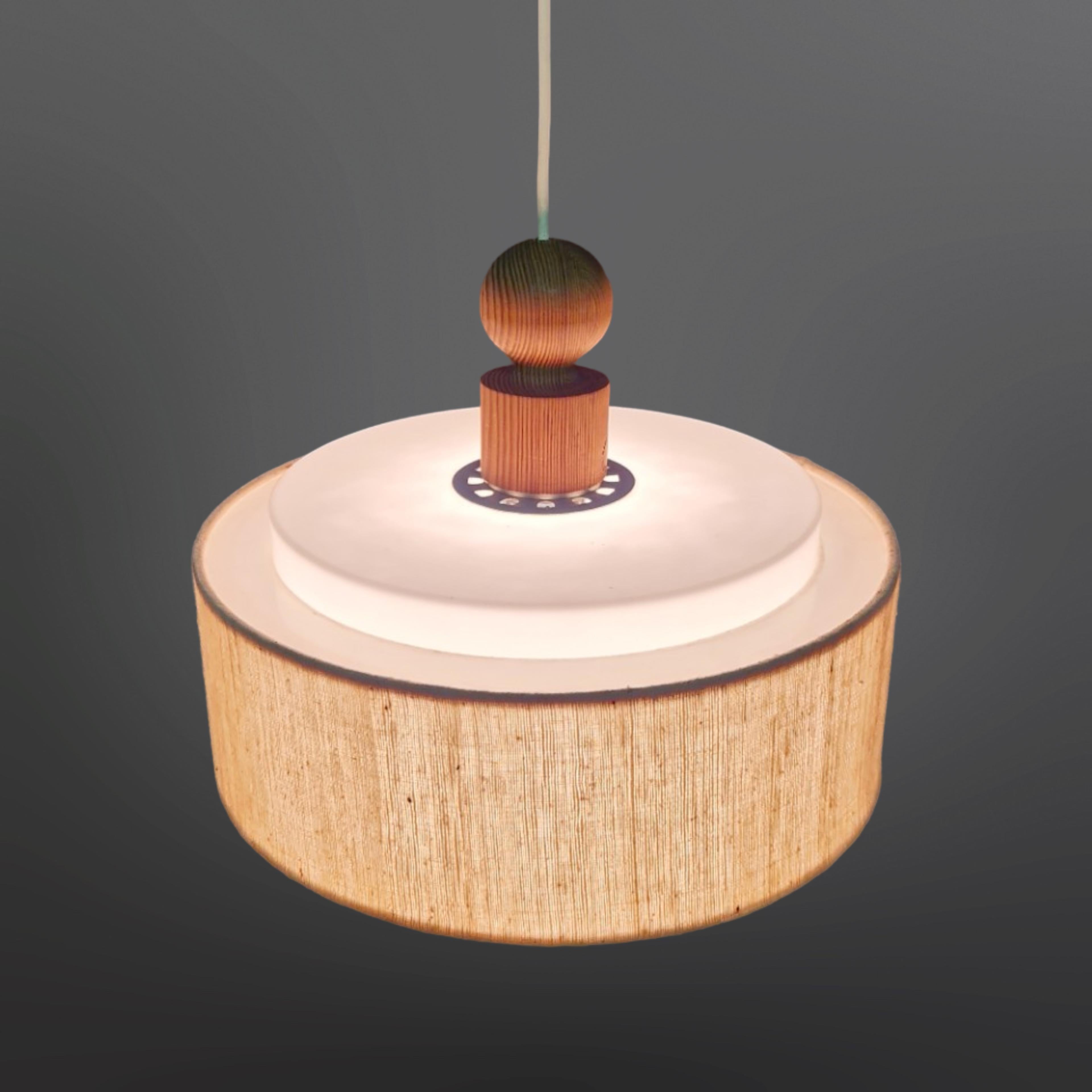 Mid century Scandinavian modern pendant lamp. Designed by Uno and Östen Kristiansson for Luxus Sweden in the 1960s. It has a pine gallery with plexiglass top and bottom diffusers and a fabric surrounding rim. 

The height is 30cm measured from the