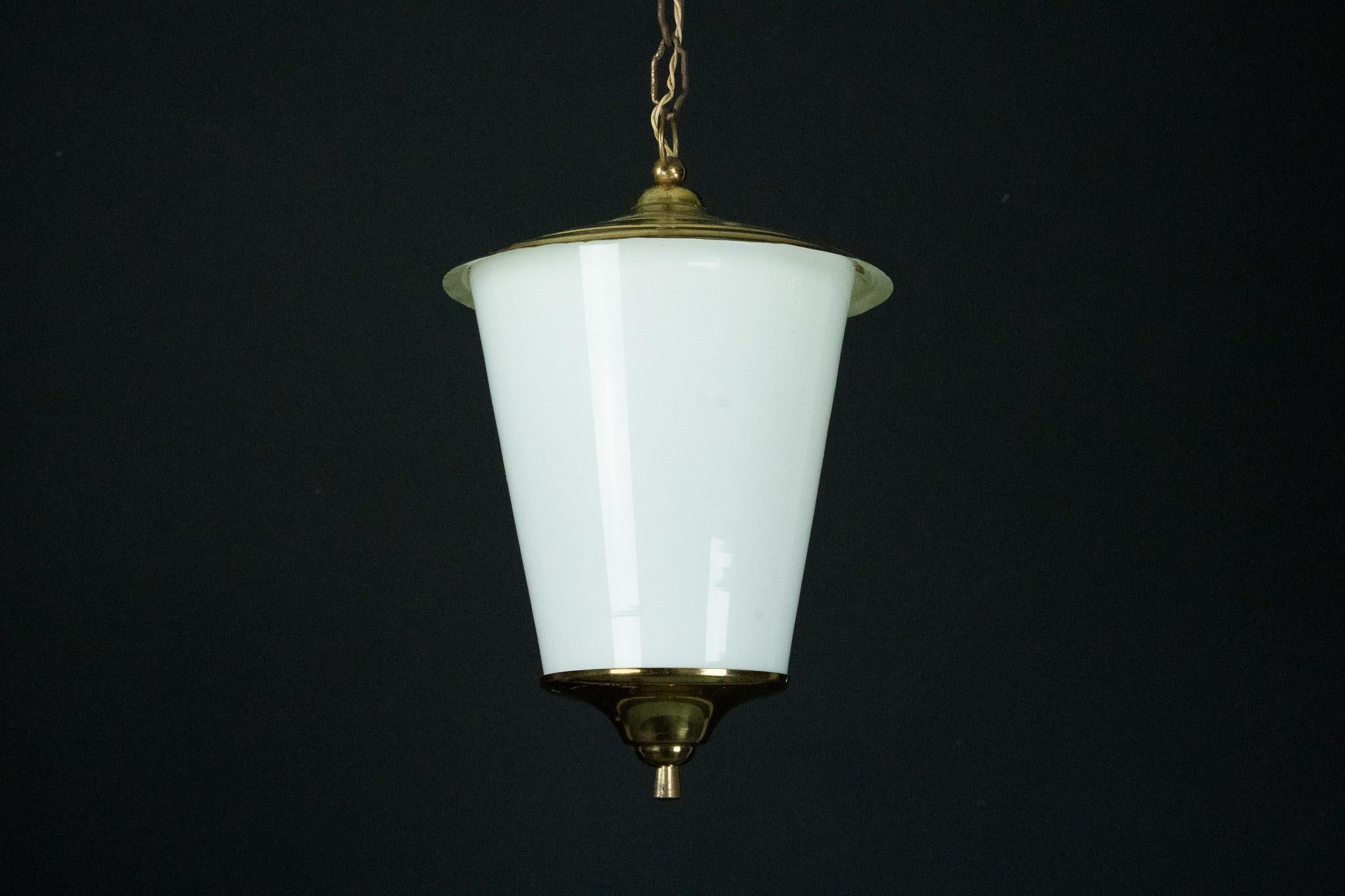 Esta elegante pieza presenta una pantalla cónica de cristal blanco lattimo (opalino), bellamente complementada con herrajes de latón pulido. El diseño refleja la refinada artesanía italiana de mediados del siglo XX, combinando líneas geométricas