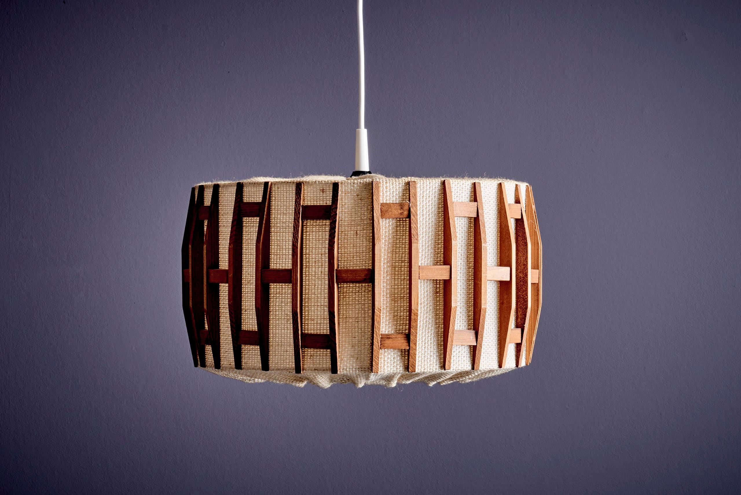 Lampe suspendue du milieu du siècle par Temde Leuchten . Avec son abat-jour cylindrique en tissu naturel tressé et ses sculpturales lamelles de teck en grille géométrique, cette pièce allie une texture organique à des lignes architecturales épurées.