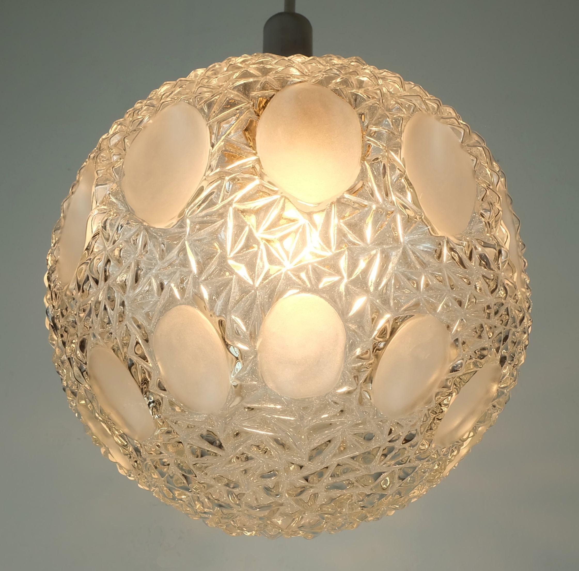 Lampada a sospensione degli anni '60-'70. Produttore Richard Essig (l'etichetta non esiste più). Paralume sferico in vetro trasparente con superficie strutturata e campi opachi incisi. Staffa, asta e tettuccio in metallo cromato. Contiene una