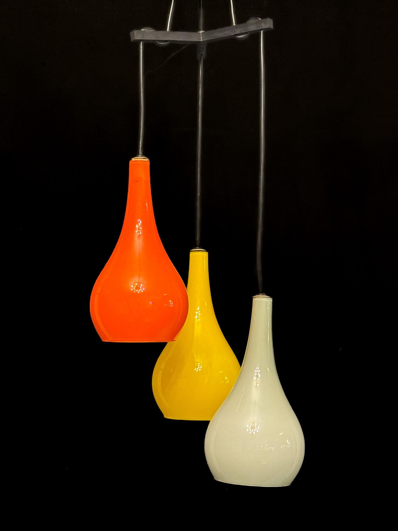 Splendide lampe suspendue du milieu du siècle conçue par Stilux Milano, dotée de trois abat-jours en verre soufflé à la main attribués à Vistosi. Chaque nuance présente une couleur distincte - orange, jaune et gris - créant une composition vibrante