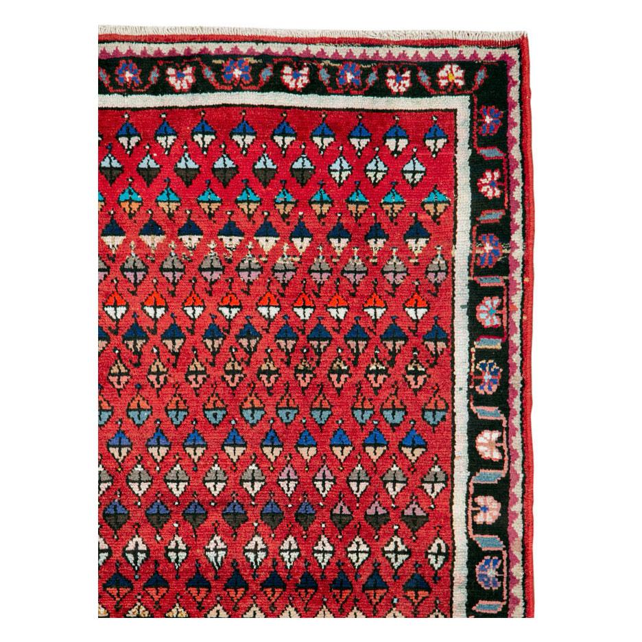 A vintage Persian Hamadan folk rug handmade during the mid-20th century in scatter/throw rug size with a red field filled with geometric botehs (paisleys).