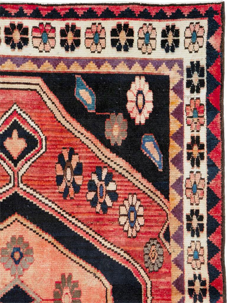 A vintage Persian Gabbeh rug from the mid-20th century. This south Persian Qashqai nomadic large scatter has a black field with corner rosettes, supporting a lightly abrashed (natural color variations) red subfield with a black and salmon pendanted