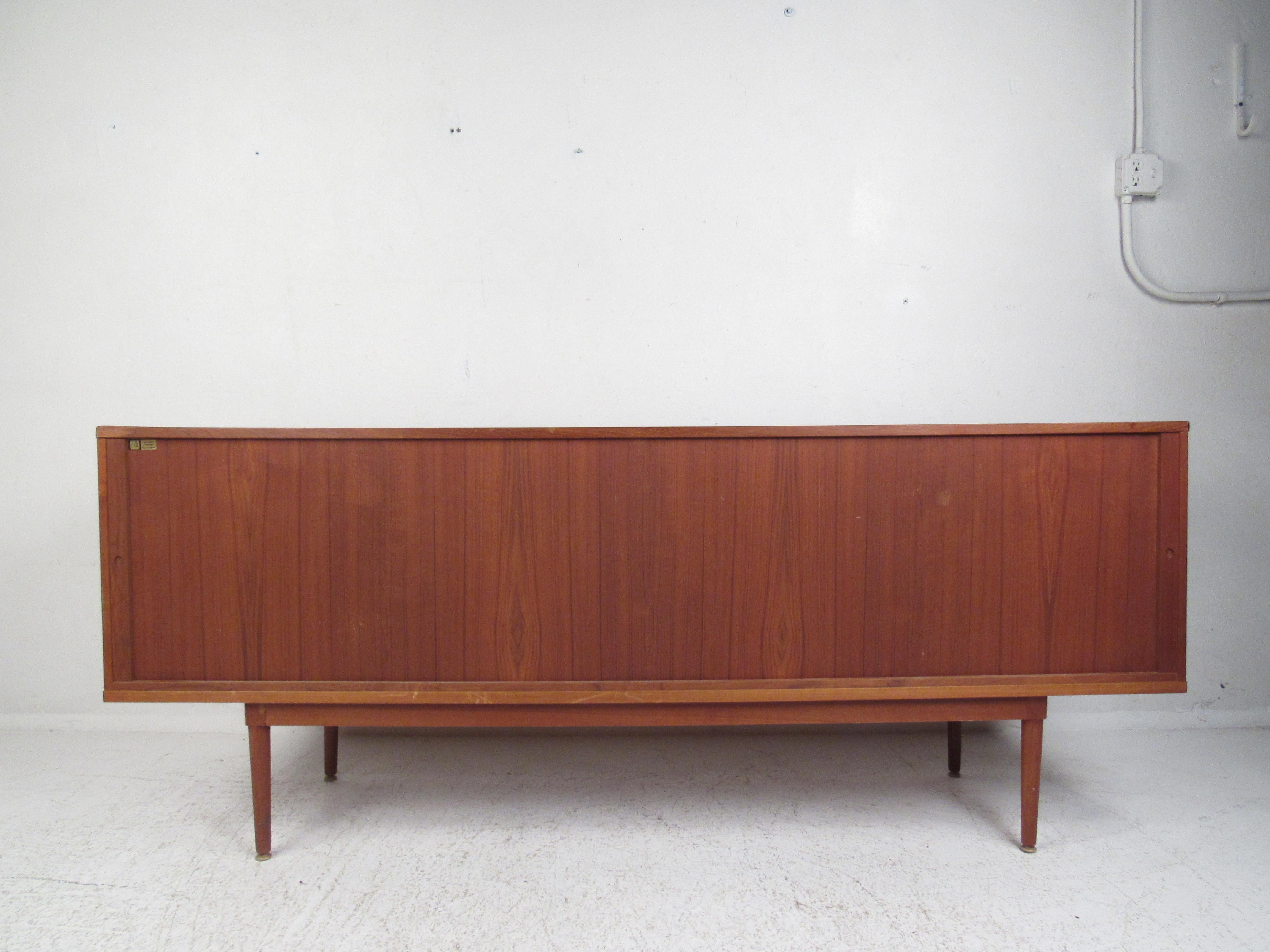 This stunning Danish modern credenza includes a topper with sliding glass doors and a base with multiple storage options. A sleek design by Peter Lovig Nielsen that boasts tambour doors with unusual handles. This well-made vintage case piece has a