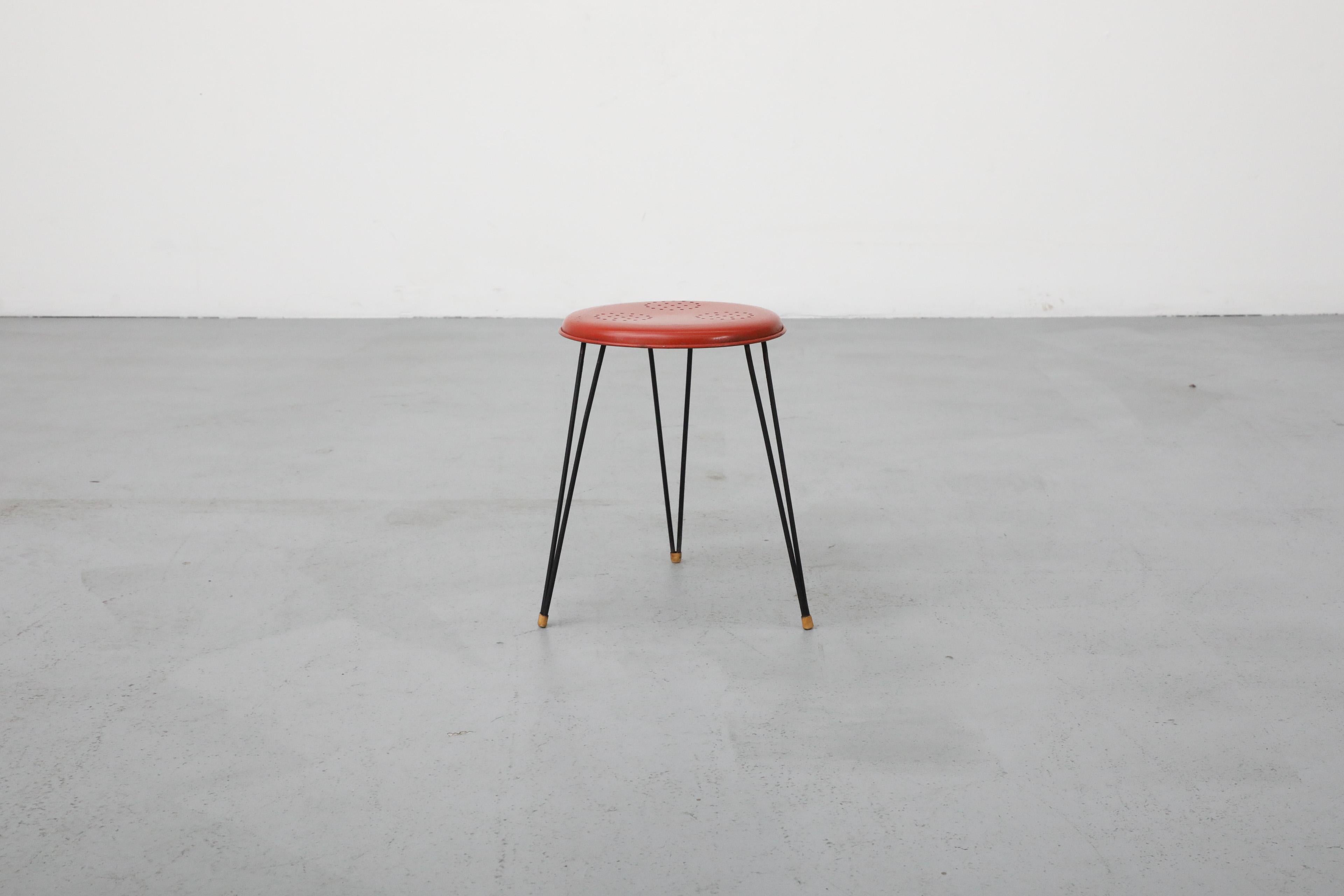This 1950's Pilastro stool has a red seat with perforated design and black hairpin legs. The stool top has a 9” diameter. In original condition with visible wear, including rust, consistent with its age and use.
