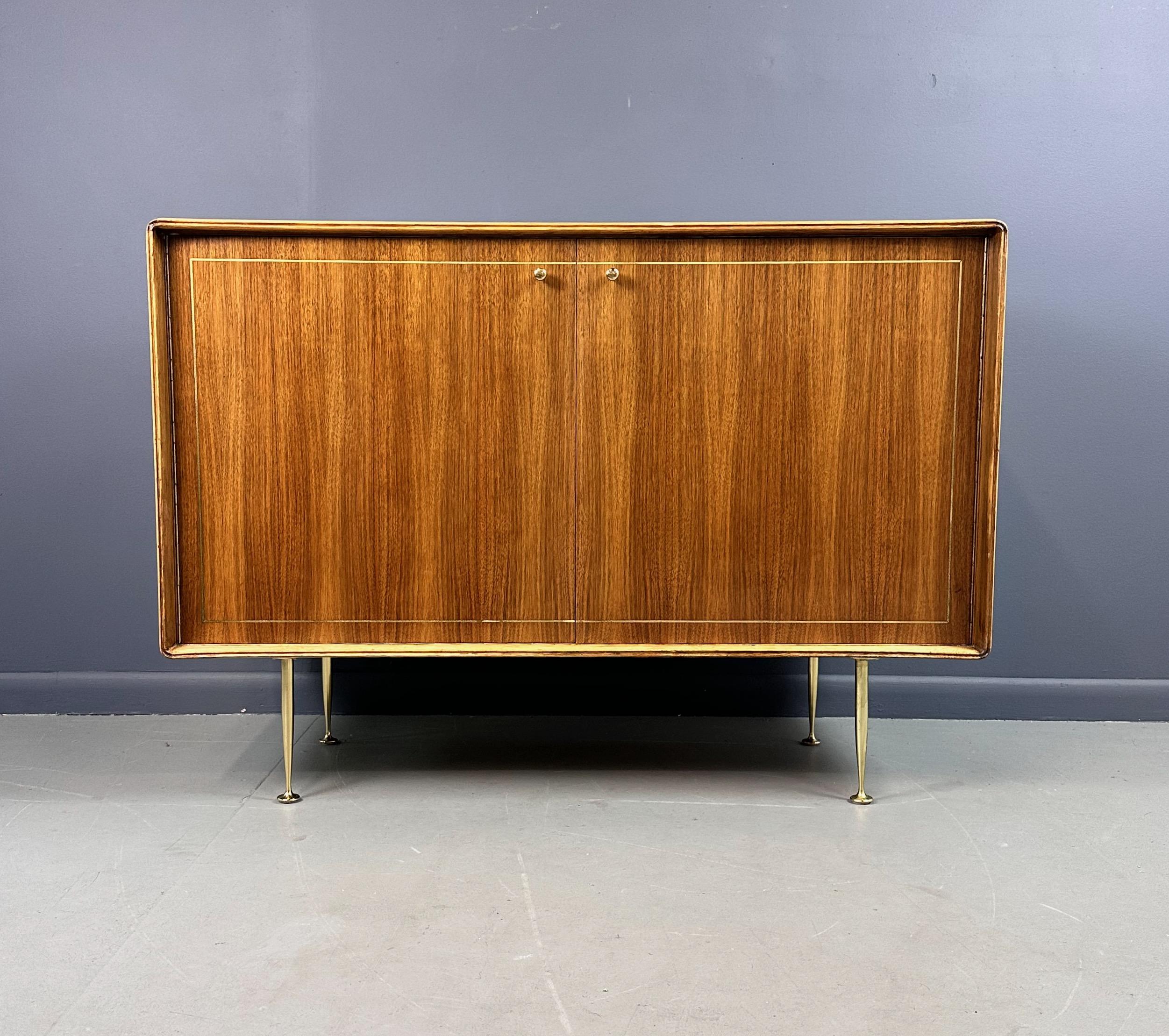 Realizzato con maestria da Erno Fabry nello stile della leggenda del design Gio Ponte, questo Petite Server del Mid Century è un'aggiunta senza tempo a qualsiasi spazio. Realizzato in Teak e Butternut, con gambe affusolate in ottone massiccio,