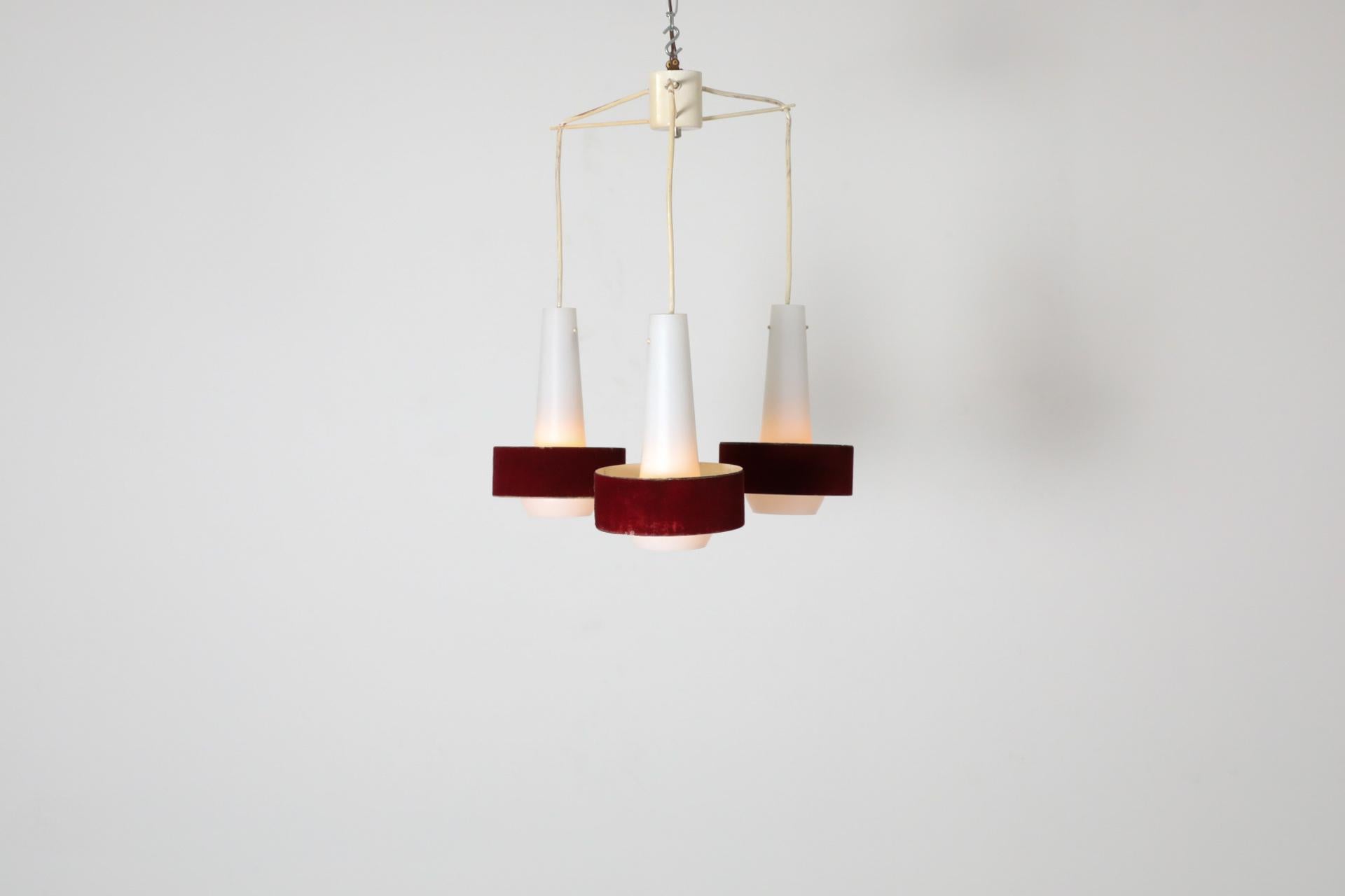 Unglaublicher Mid-Century-Kronleuchter mit einem Trio von Milchglasschirmen mit gebänderten roten Samtringen. Die Anhänger sind an drei separaten Armen befestigt, die von der Basis ausgehen. Die Leuchte befindet sich im Originalzustand mit