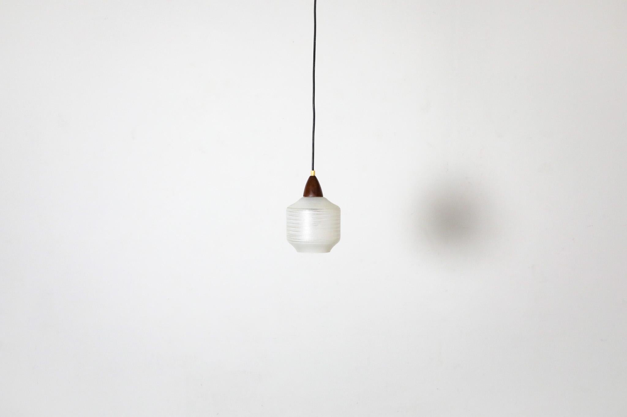 Lampada a sospensione di metà secolo, in teak e vetro a righe. Il paralume a righe ha una superficie strutturata in rilievo ed è sostenuto da un cono in teak. Una bella e delicata lampada a sospensione in condizioni originali, con qualche segno di