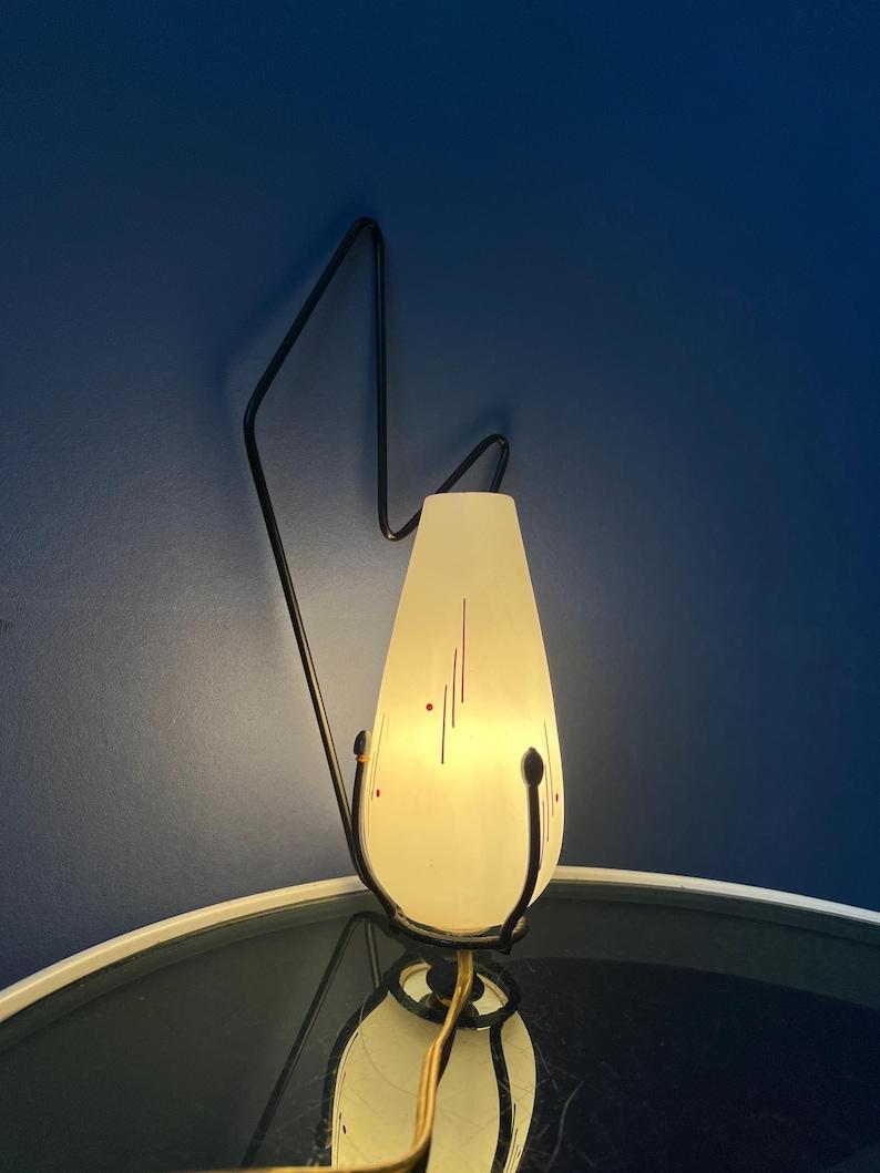 Lámpara ovalada de pared o sobremesa de cristal de leche de mediados de siglo, de Philips. La pieza tiene un marco de metal negro que se puede colgar en la pared. También puede colocarse sobre una mesa o escritorio. La pieza tiene forma de tulipán