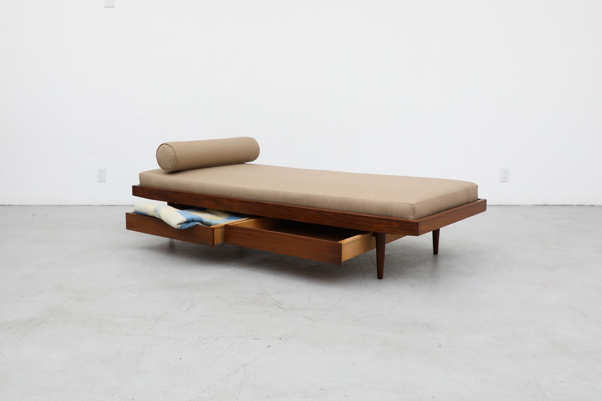 Beautiful midcentury teak daybed with new taupe upholstered mattress and bolster. A sleek modern design with two lower storage drawers, a raised edge frame, inset pegboard support, and tapered teak legs. The frame has been lightly refinished with