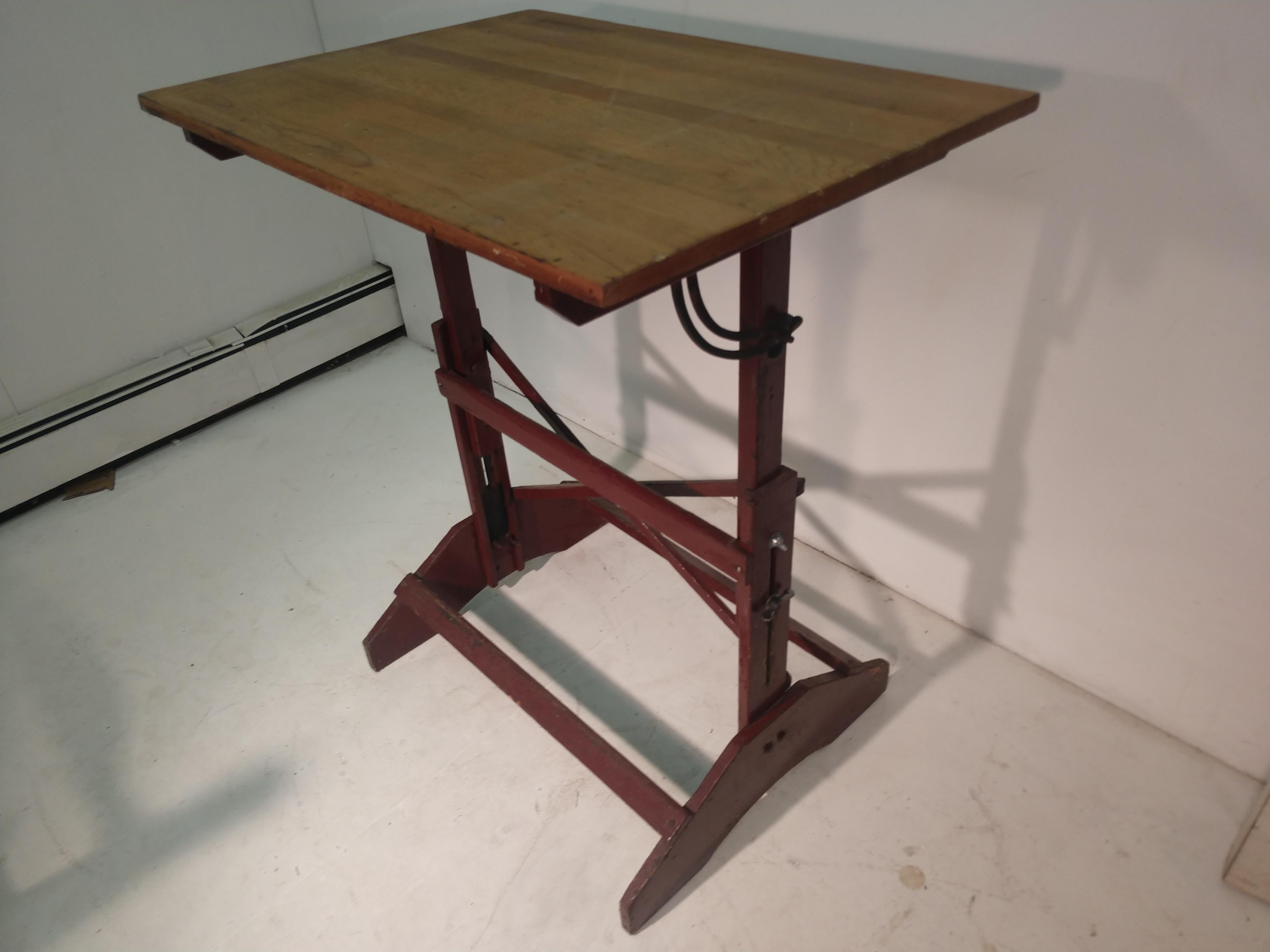 Fully adjustable drafting table in pine. Lightweight for maneuverability. Base is painted a reddish brown. Lowers to 31 inches in hgt. Excellent standing desk to work at.