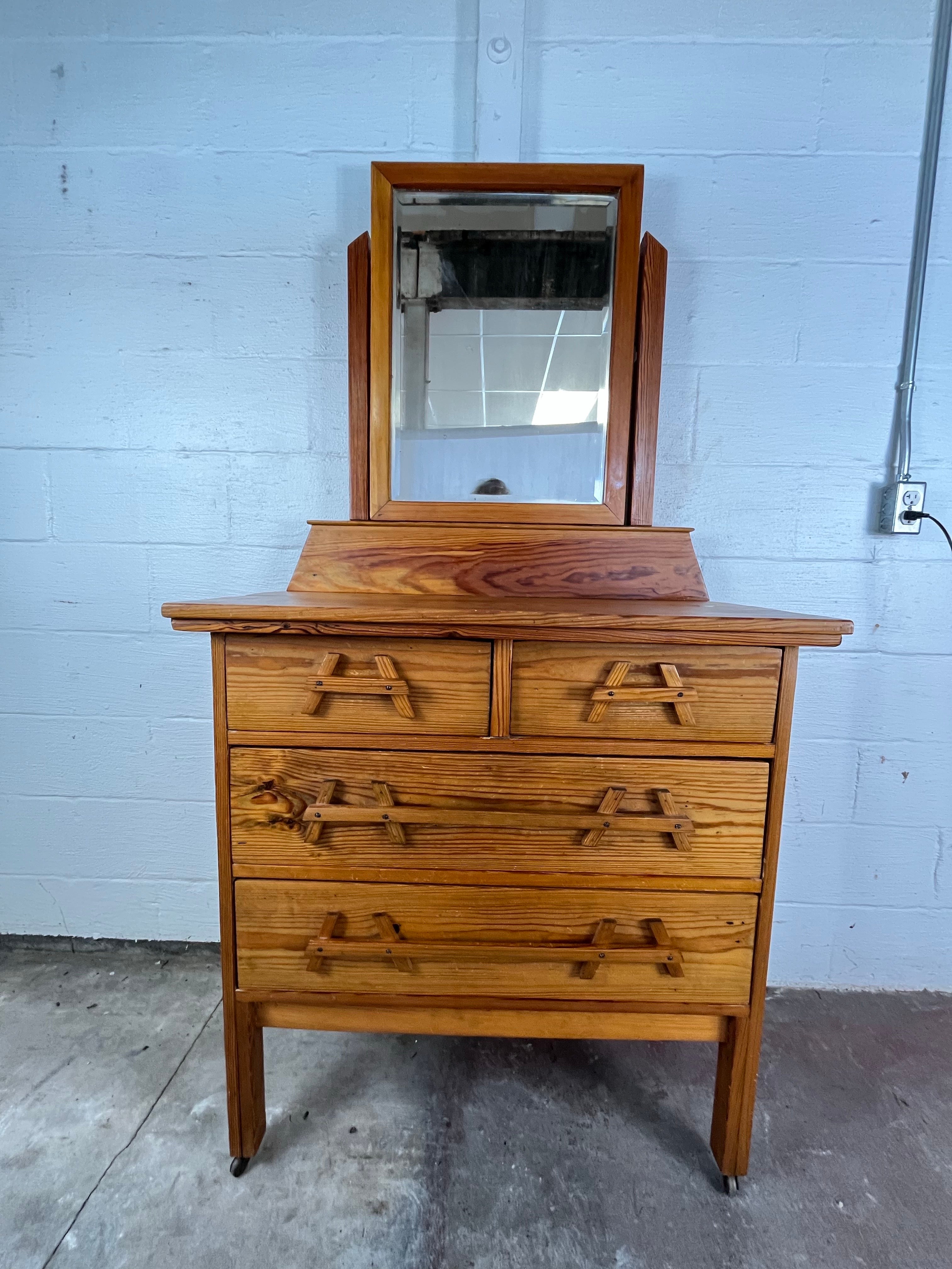 Questo comò in pino della metà del secolo scorso presenta linee pulite, venature naturali e scultorei tiranti in legno a forma di telaio ad A che aggiungono un sottile tocco artigianale. Lo specchio girevole integrato poggia su un'elegante galleria