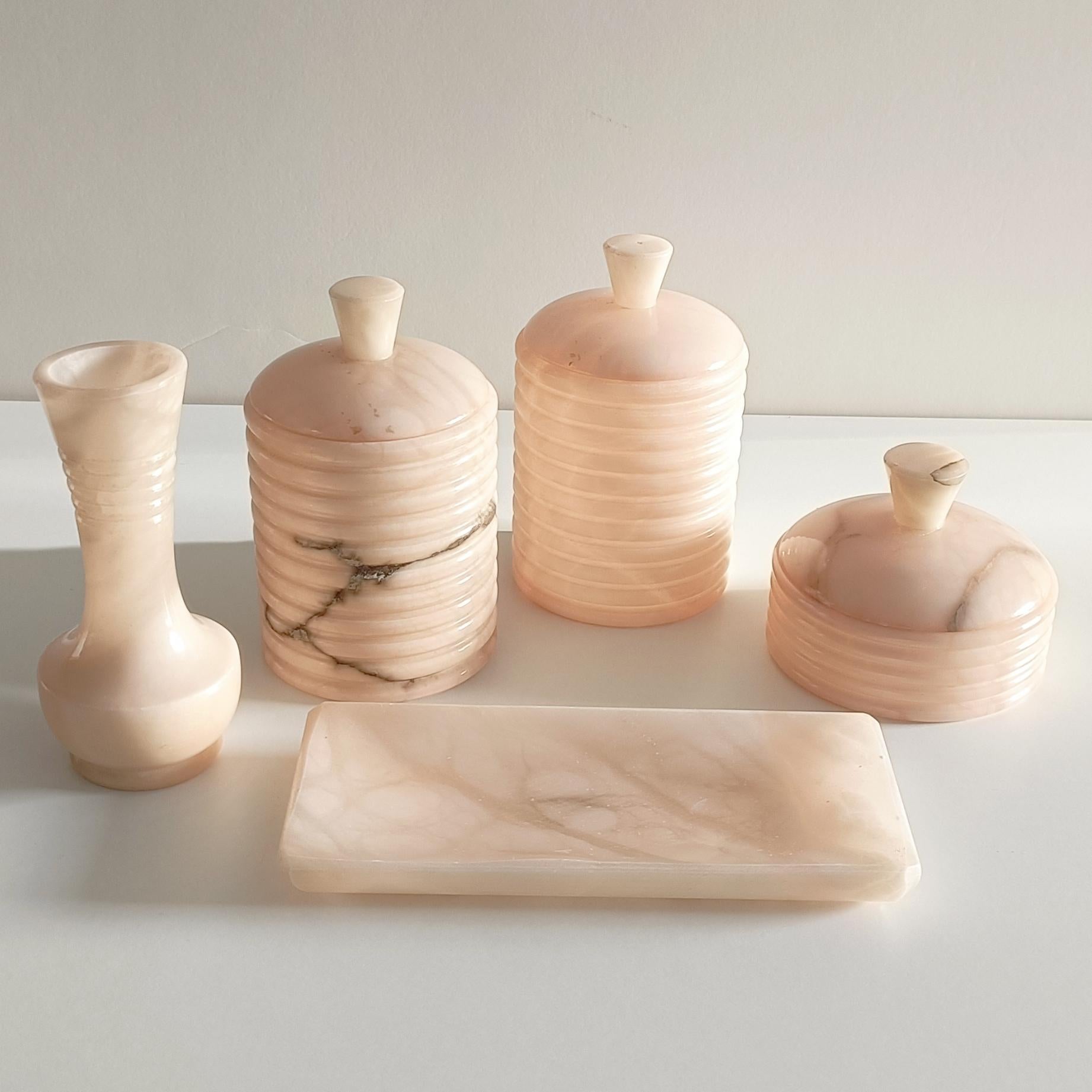 A very beautiful Art Deco bathroom or vanity set made from pink alabaster, handmade in Spain circa the 1940s. 

The set includes five pieces: two taller lidded jars, one shorter lidded jar, a soap or jewelry tray, and a ¨soliflower¨ vase. 

Each