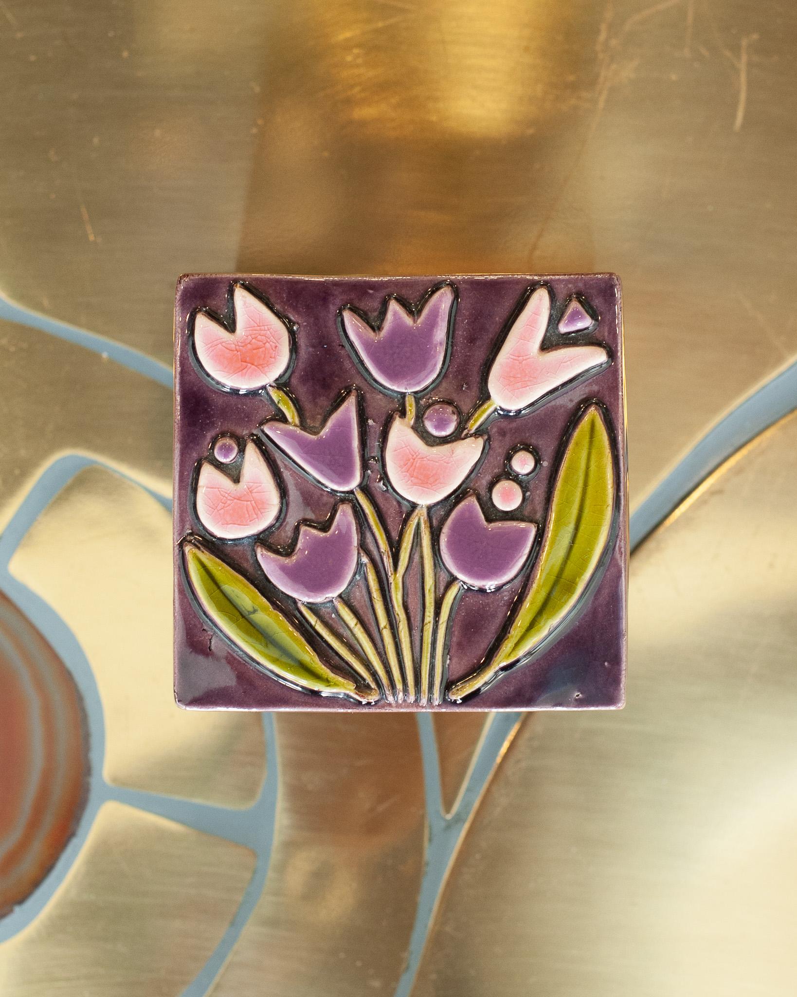 Un'eccezionale scatola in ceramica smaltata di metà secolo con fiori viola e rosa, opera della famosa artista Mithé Espelt. Il coperchio della scatola è in ceramica con una base in legno annerito.
Nata nel 1923, Mithé Espelt era un'artista della