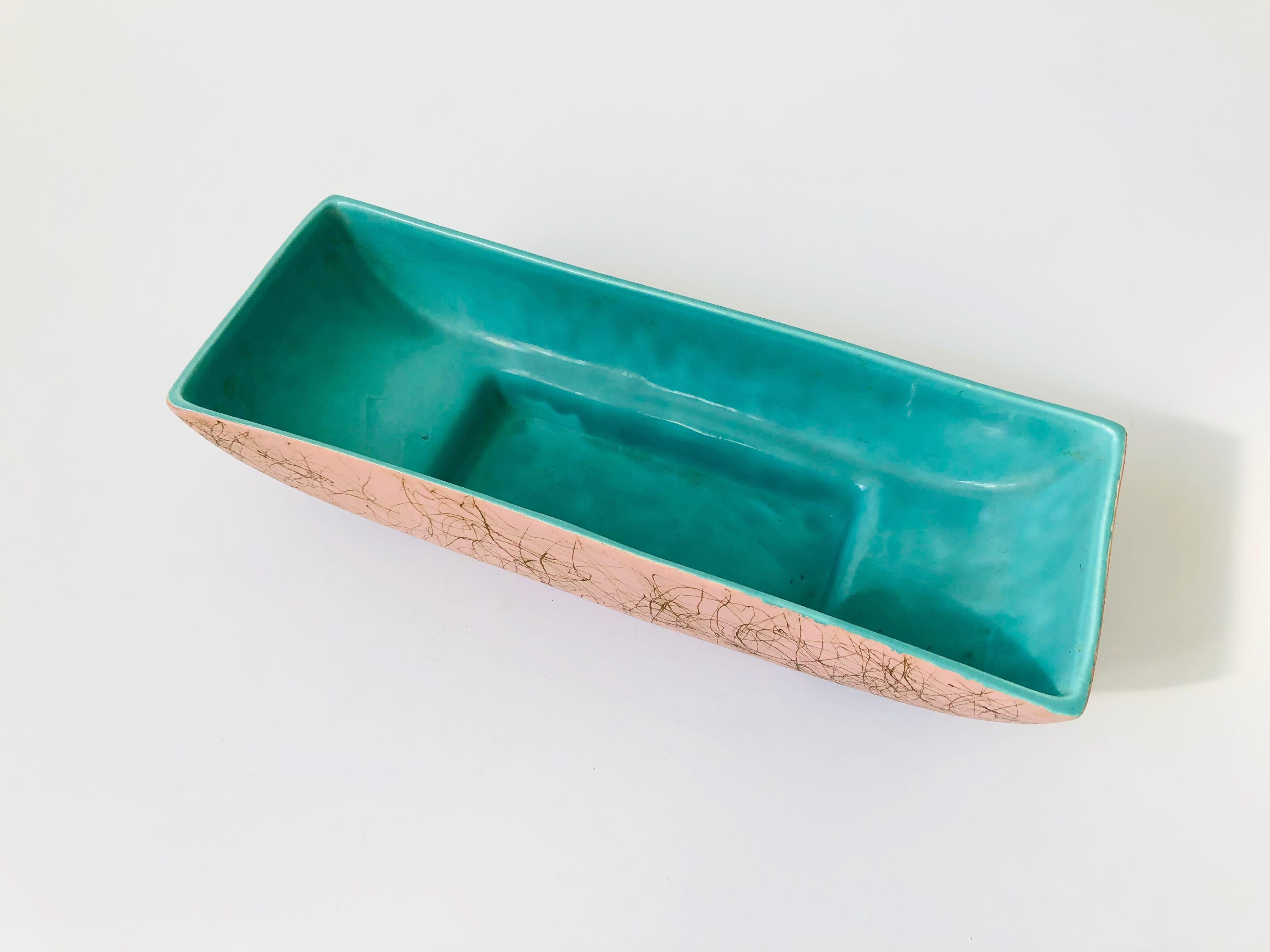 A mid-century pottery planter bowl made by Maddux of California. Nice long rectangular shape, perfect for using as a centrepiece. Light pink exterior glaze with a freeform gold squiggle pattern and a contrasting bright turquoise interior.
 