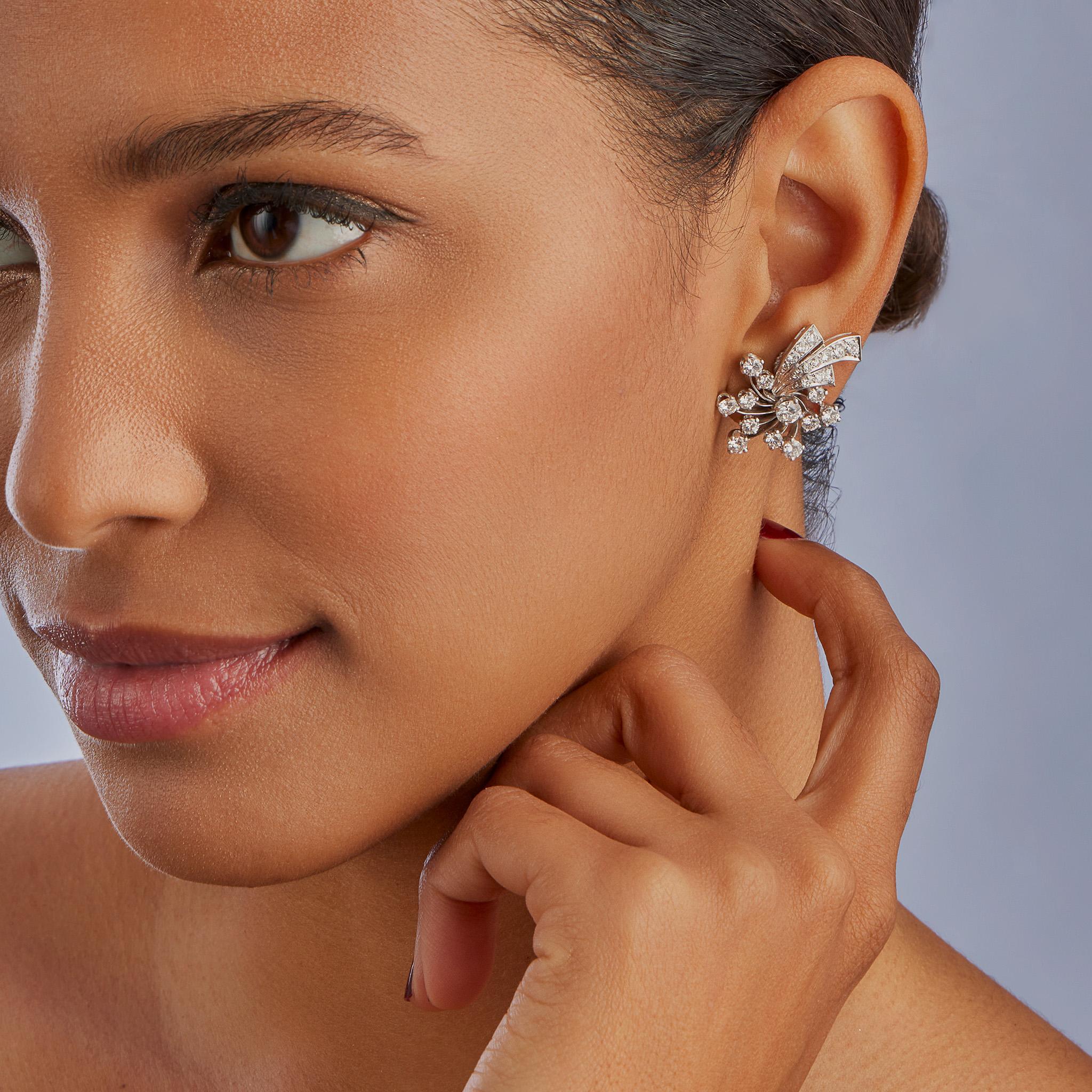 Created in the 1950s, these diamond clip earrings are set in platinum. The stylized forms set throughout with round brilliant-cut diamonds are designed as a floral spray on delicate swirling filaments, joining upward sweeping stems. A classic,