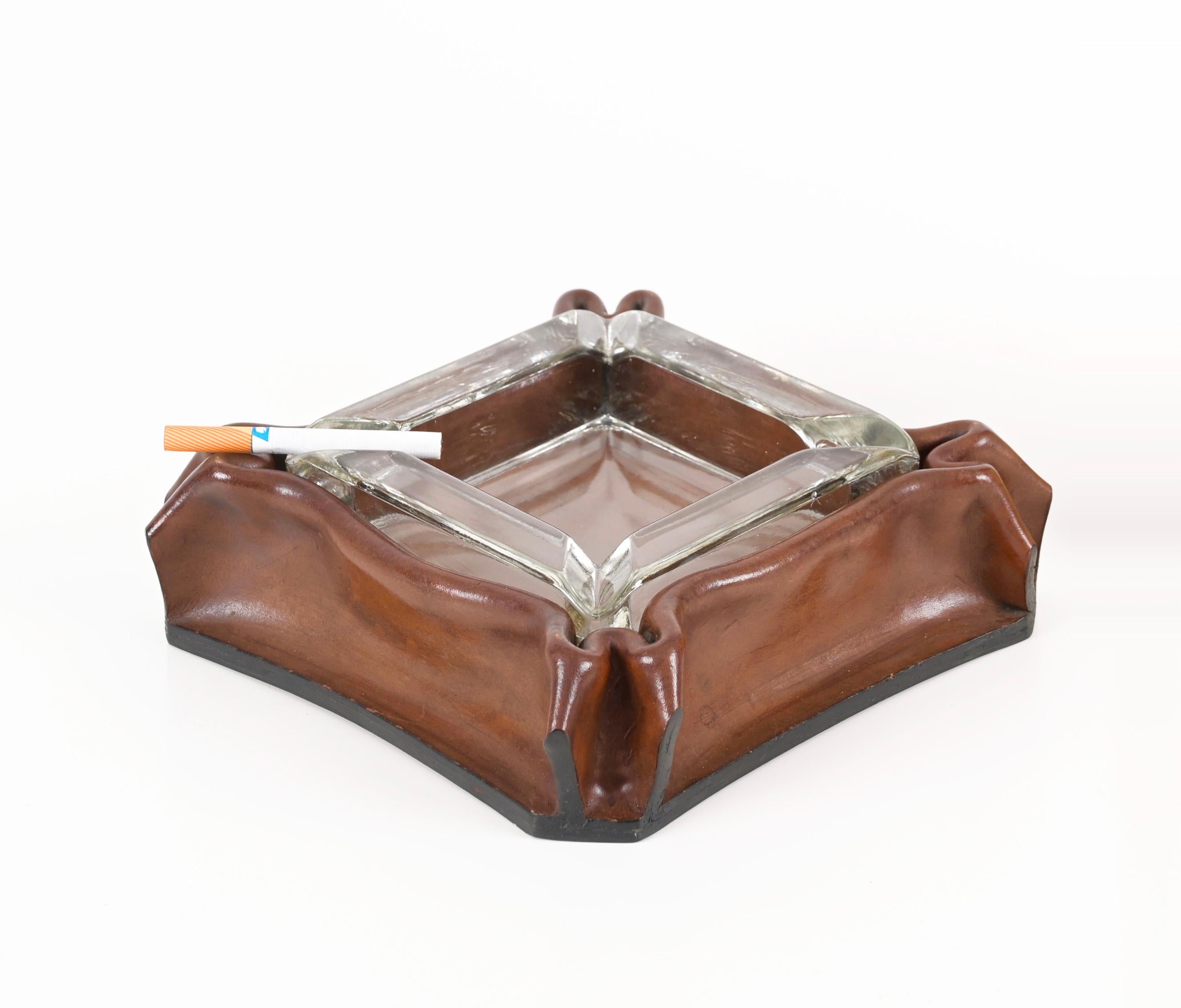 Stunning ashtray with pleated leather frame and crystal glass. This charming ashtray was designed by Jacques Adnet and produced in Italy during the 1970s, it is signed on the bottom. 

This elegant ashtray has an external frame fully made in a