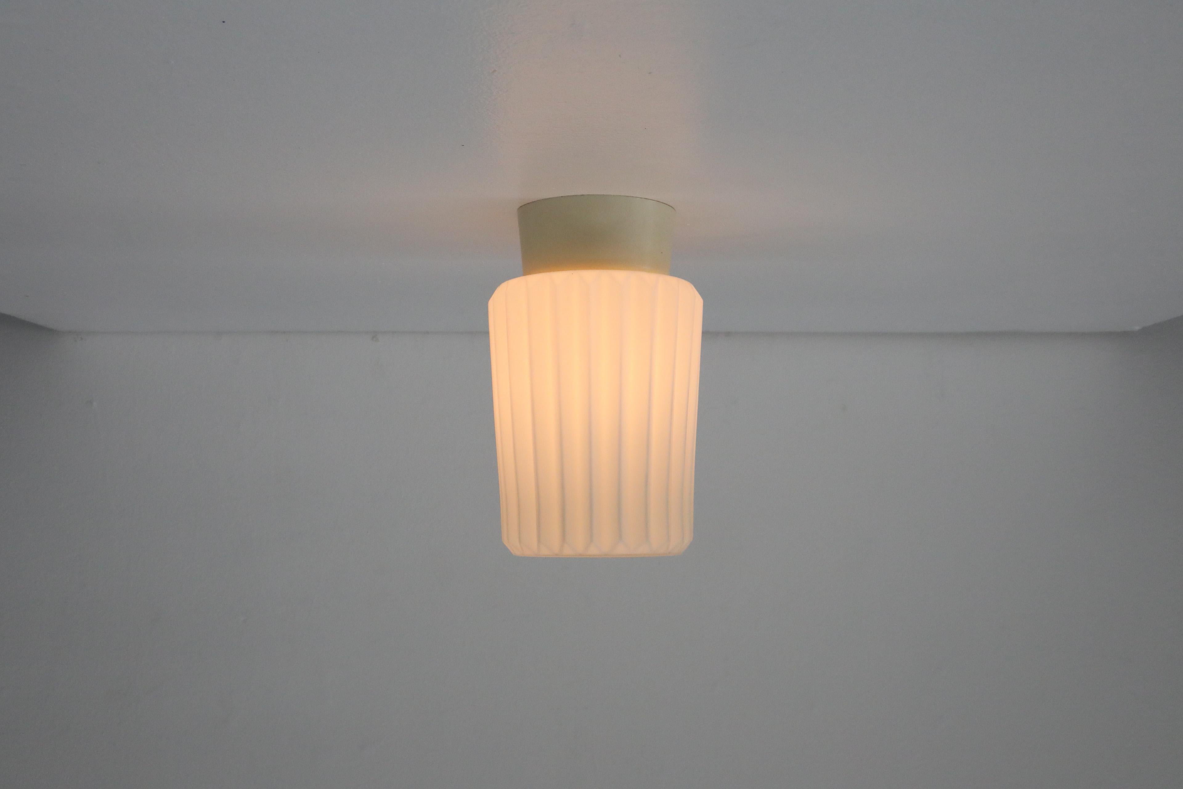 Delicata applique da soffitto olandese di metà secolo con paralume tubolare in vetro latte plissettato bianco montato su una base in bachelite color crema. In condizioni originali con qualche segno di usura dovuto all'età. Per l'installazione a filo.