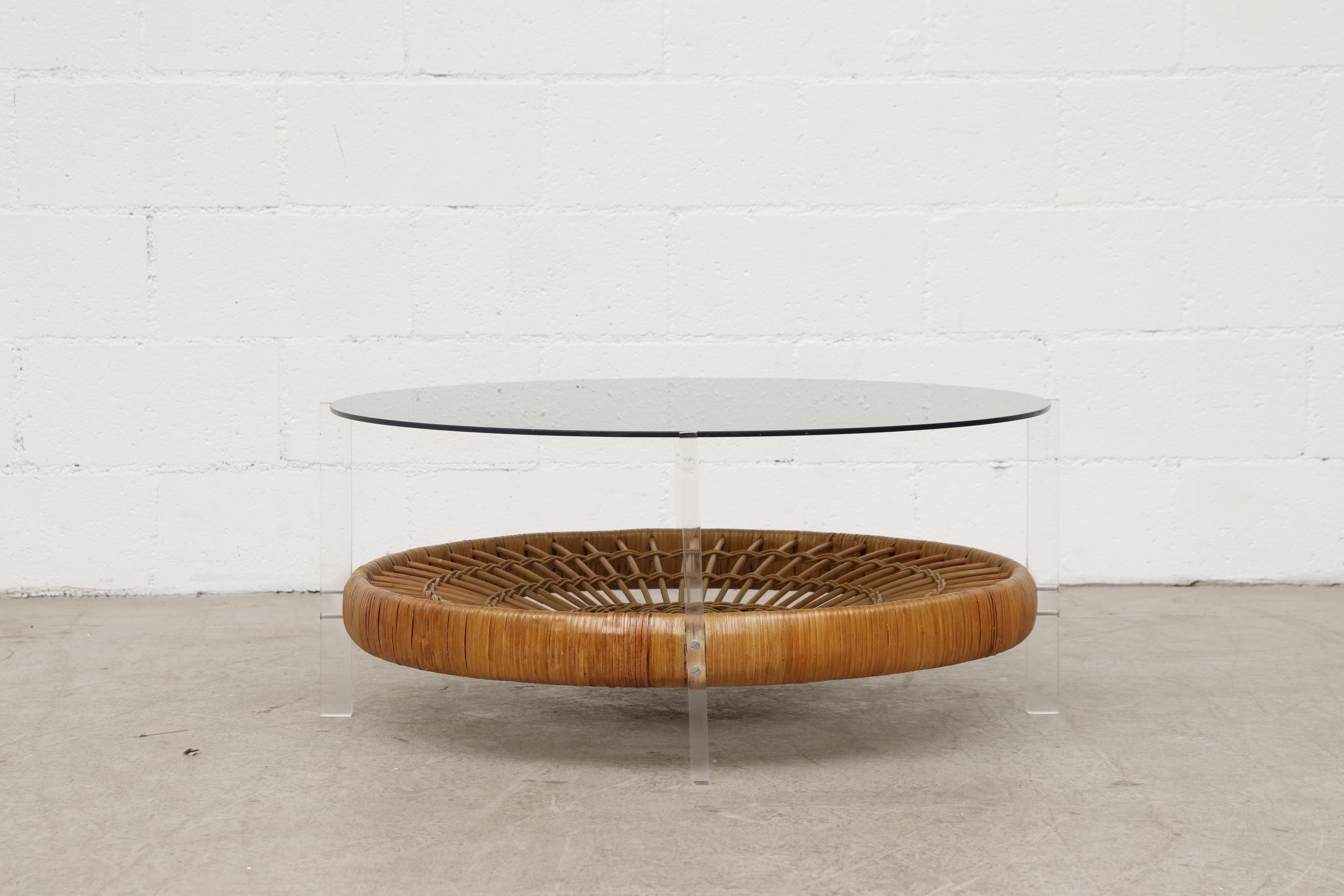 MOD round smoked glass coffee table with plexiglass legs and lower rattan basket. In original condition with normal wear and visible scratching to the glass top. Glass is 35.325