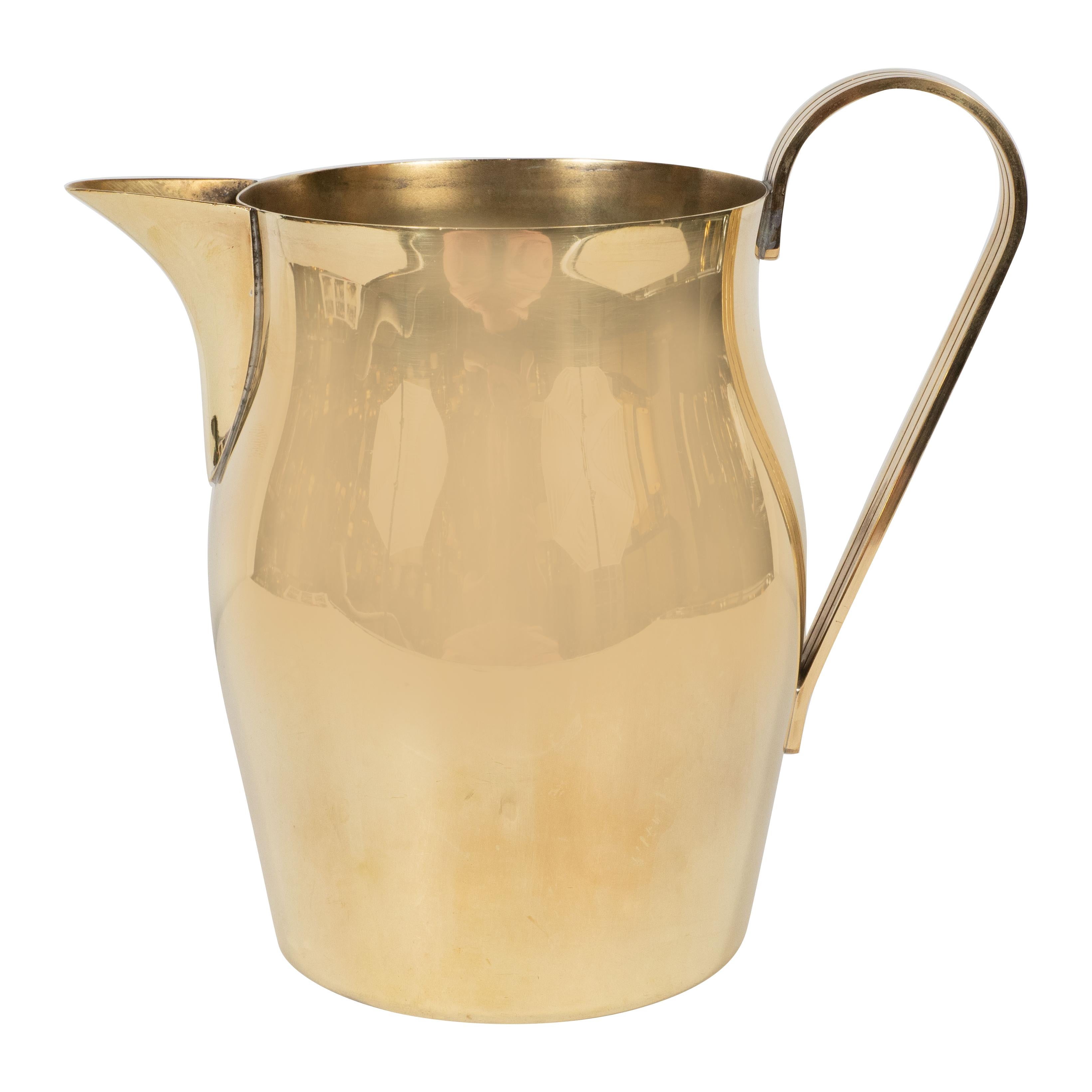 This elegant Mid-Century Modern pitcher was realized by the celebrated 20th century designer Tommi Parzinger, circa 1950. It features a undulating cylindrical body, a streamlined and striated handle with two engraved lines in the center and peaked