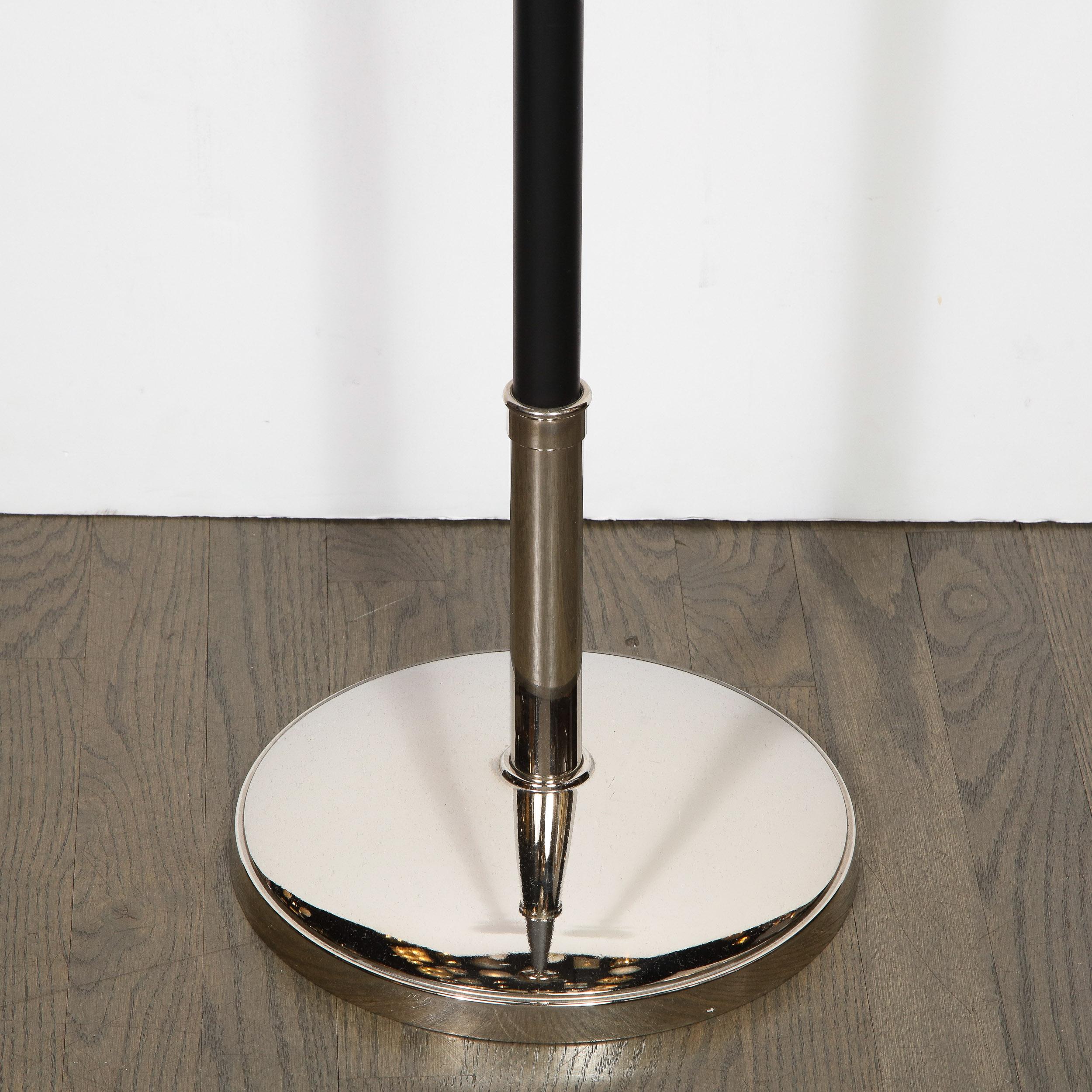 This refined Mid-Century Modern floor lamp was realized in the United States, circa 1950. Designed in the manner of Tommi Parzinger, the floor lamp features a circular polished nickel base; a black enamel body; a channeled conical neck; a bell