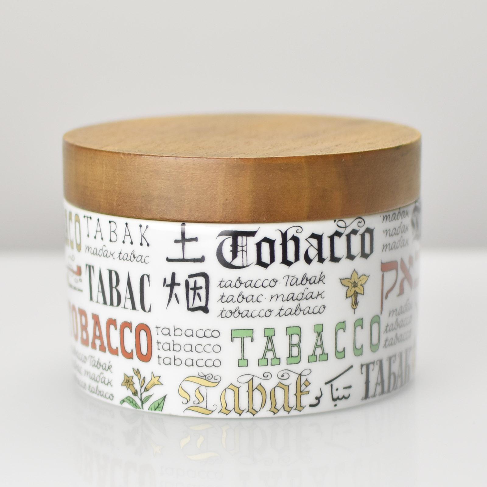 This mid-century modern tobacco jar features an eye-catching porcelain base adorned with multilingual typography spelling out 