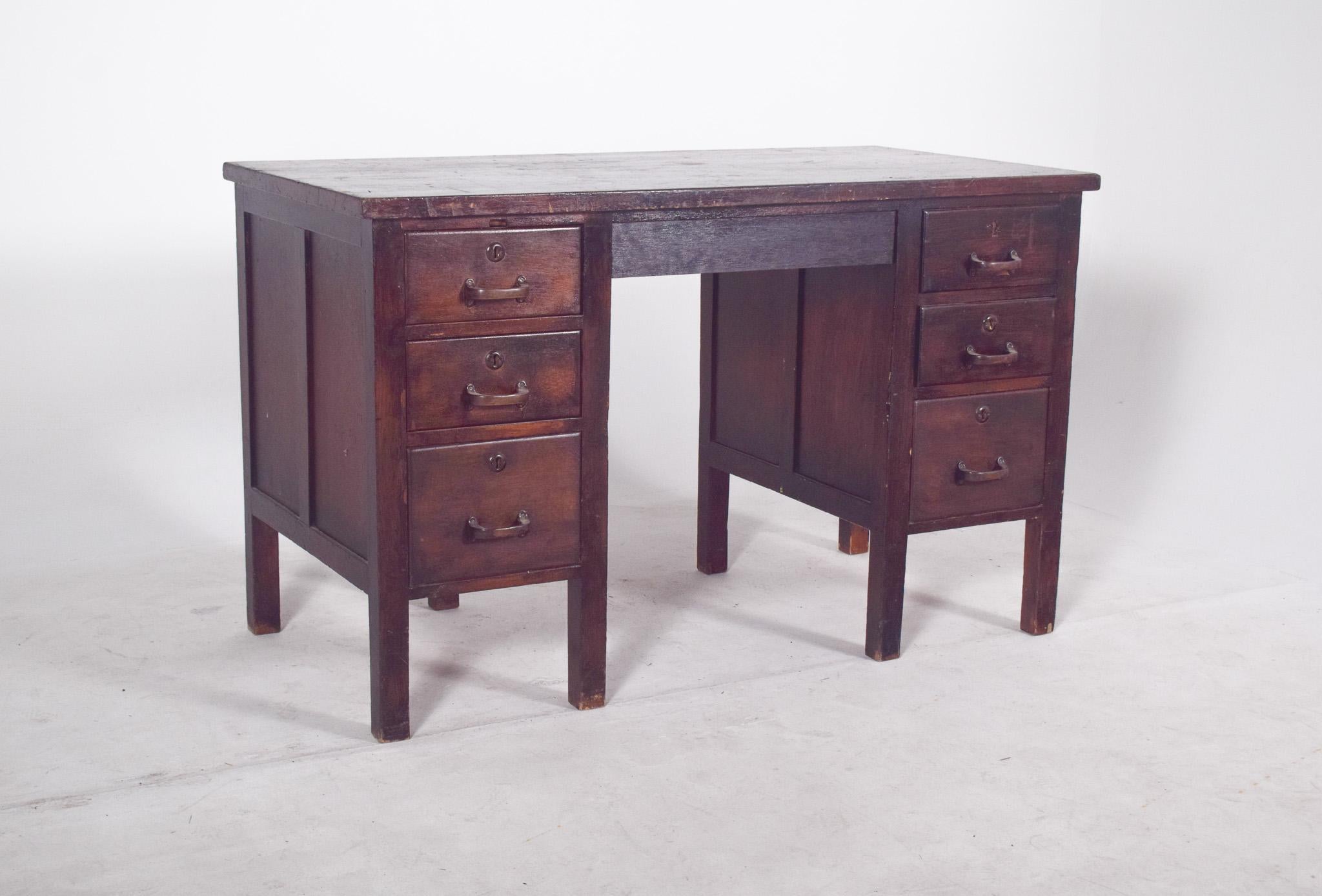 Scrivania portoghese della prima metà del XX secolo. In legno scuro, con una struttura simmetrica e funzionale, tipica dei mobili da ufficio del XX secolo. Presenta due colonne laterali, ognuna con quattro cassetti con maniglie in metallo in uno